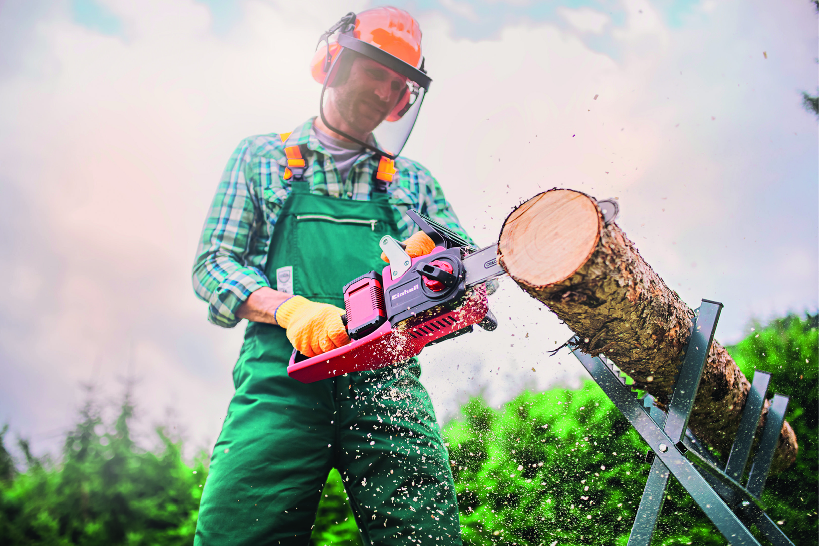 Osoba używająca czerwonej piły łańcuchowej Einhell do cięcia kłody na koziołku. Osoba nosi sprzęt ochronny.