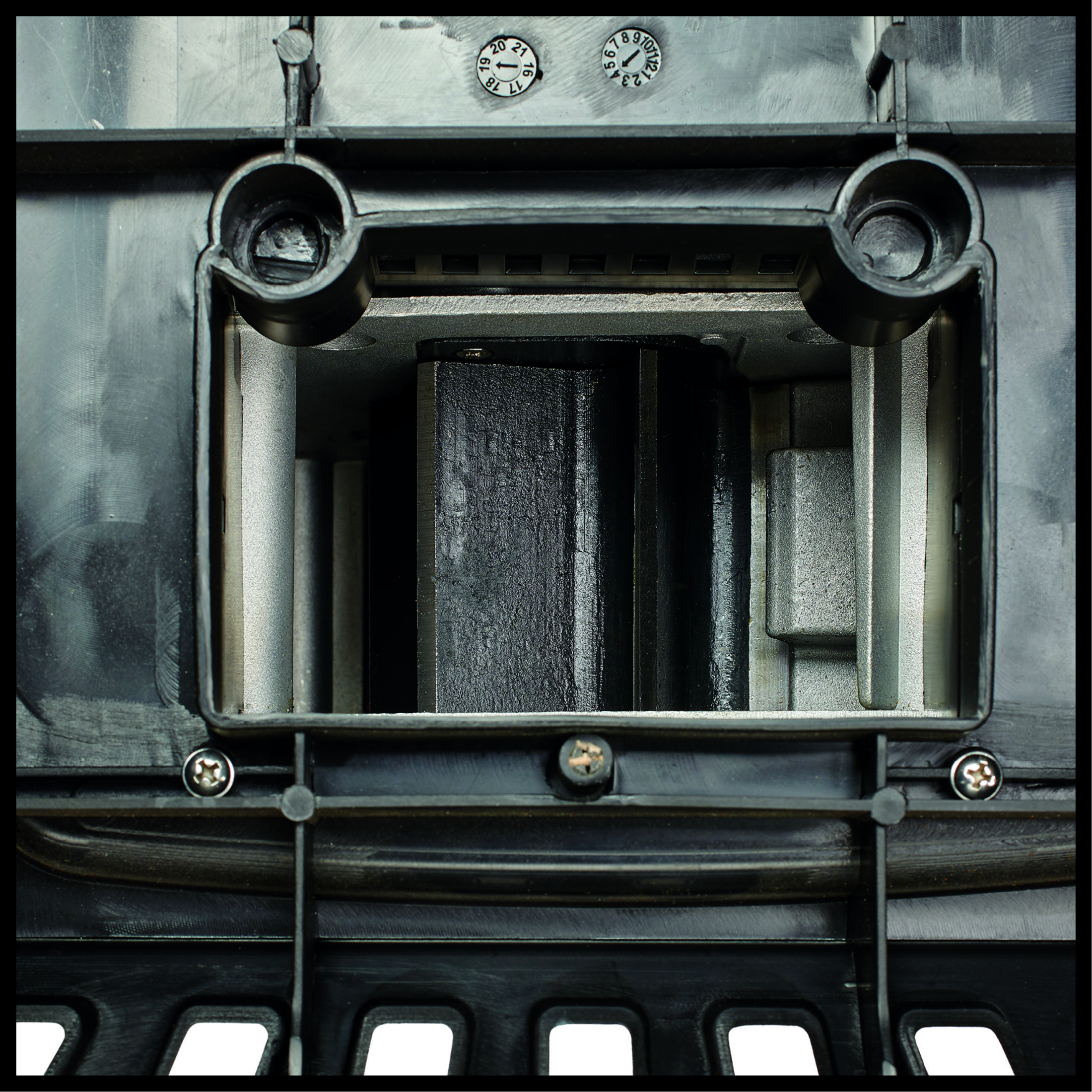 Nahaufnahme des Inneren eines schwarzen Mechanismus. Enthält ein Zifferblatt und Metallelemente.