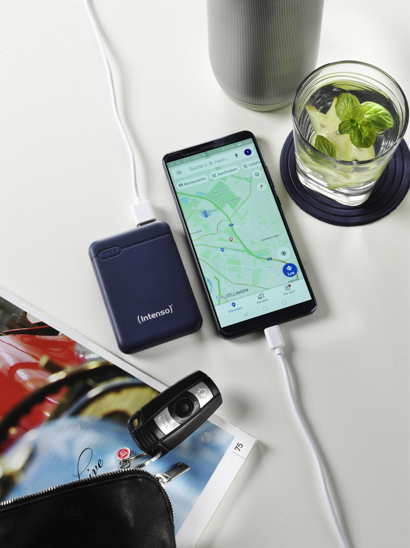Un power bank che carica un telefono. Una chiave dell'auto e una borsa sono su un tavolo con una bevanda.