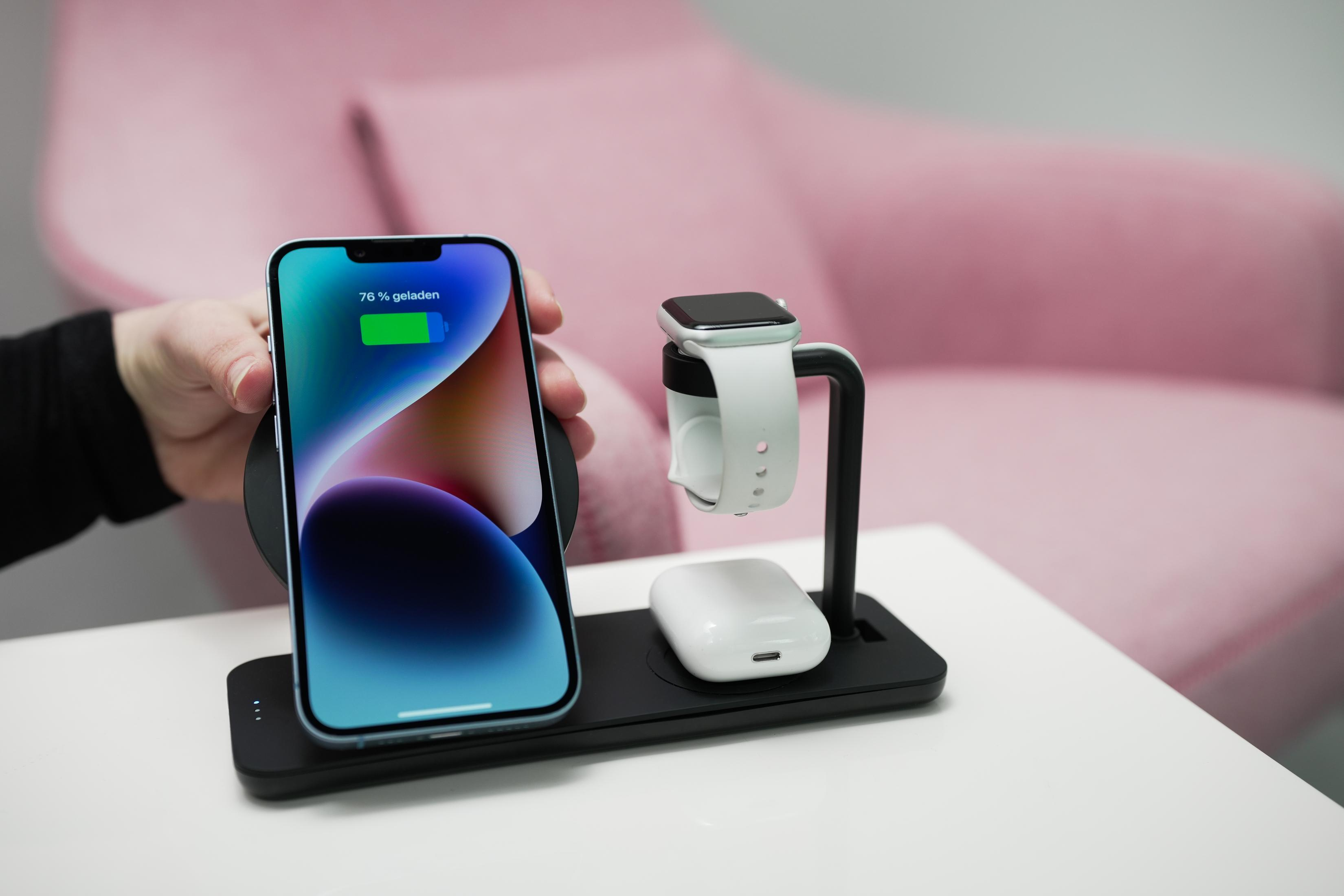 Eine Ladestation mit Telefon, Smartwatch und Ohrhörern. Telefon zeigt 76% Ladung auf rosa Hintergrund.