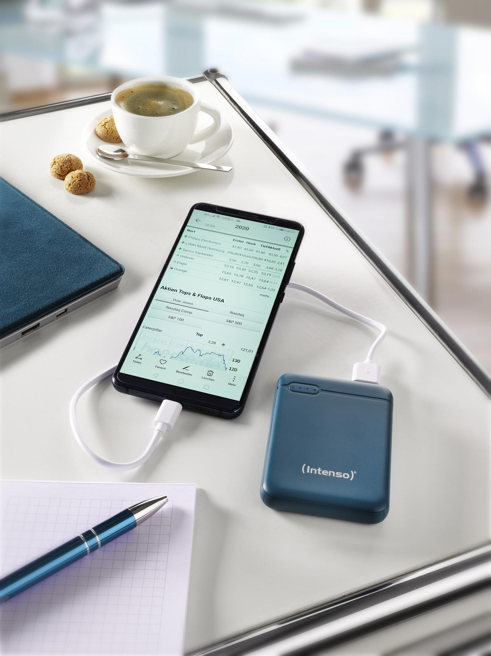 Ein Telefon, das von einer Intenso Powerbank geladen wird. Ein Stift, ein Notizbuch und Kaffee auf dem Tisch.