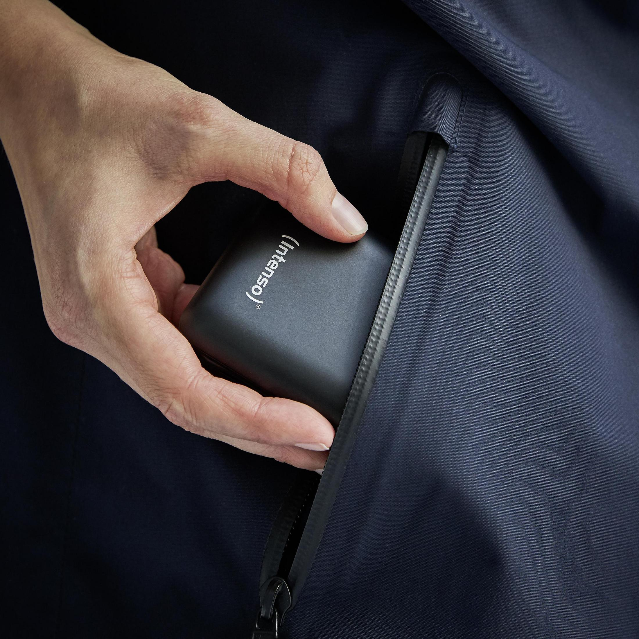 Mano insertando batería externa negra en bolsillo de chaqueta azul marino.