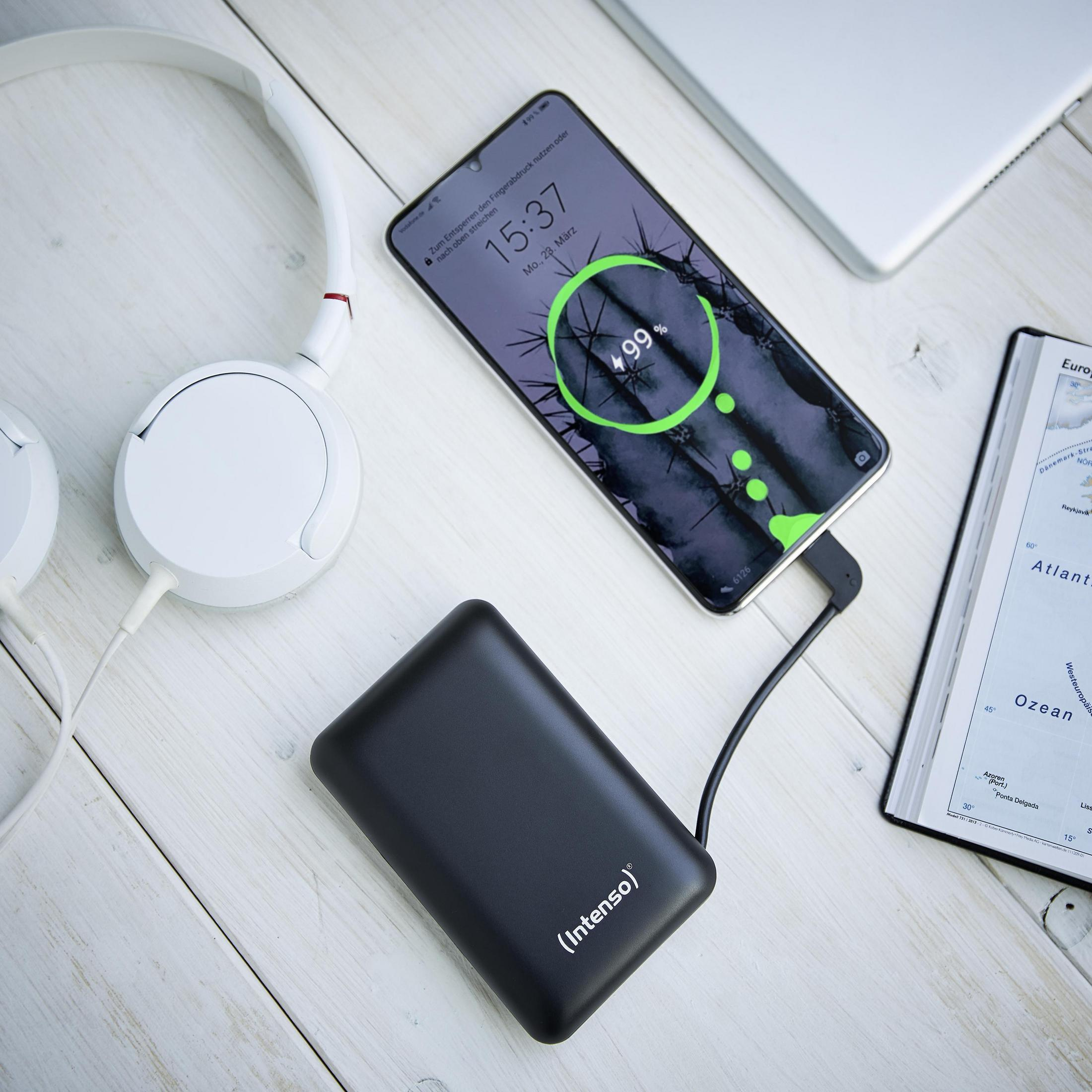 Banco de energía negro cargando un teléfono. El teléfono muestra el 99% de carga. Auriculares y un mapa en la mesa.
