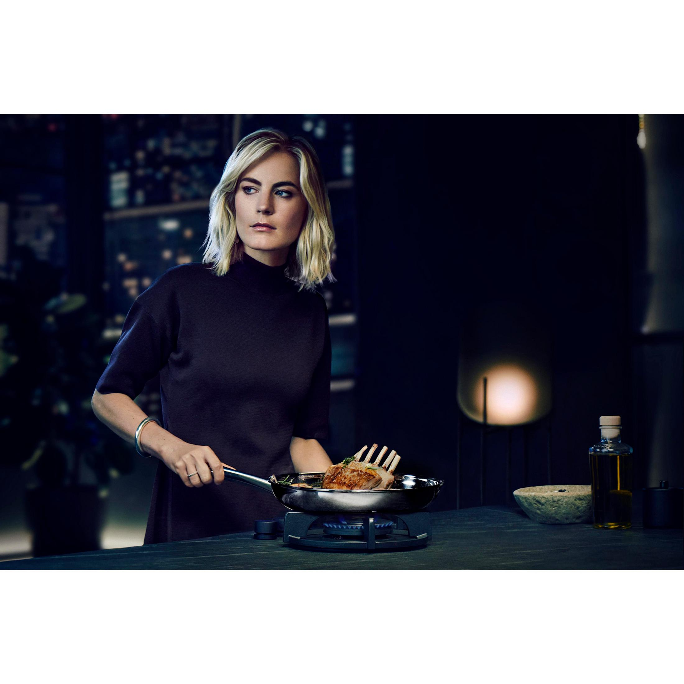 Kobieta gotuje na patelni z jedzeniem na kuchence, w ciemnym otoczeniu.