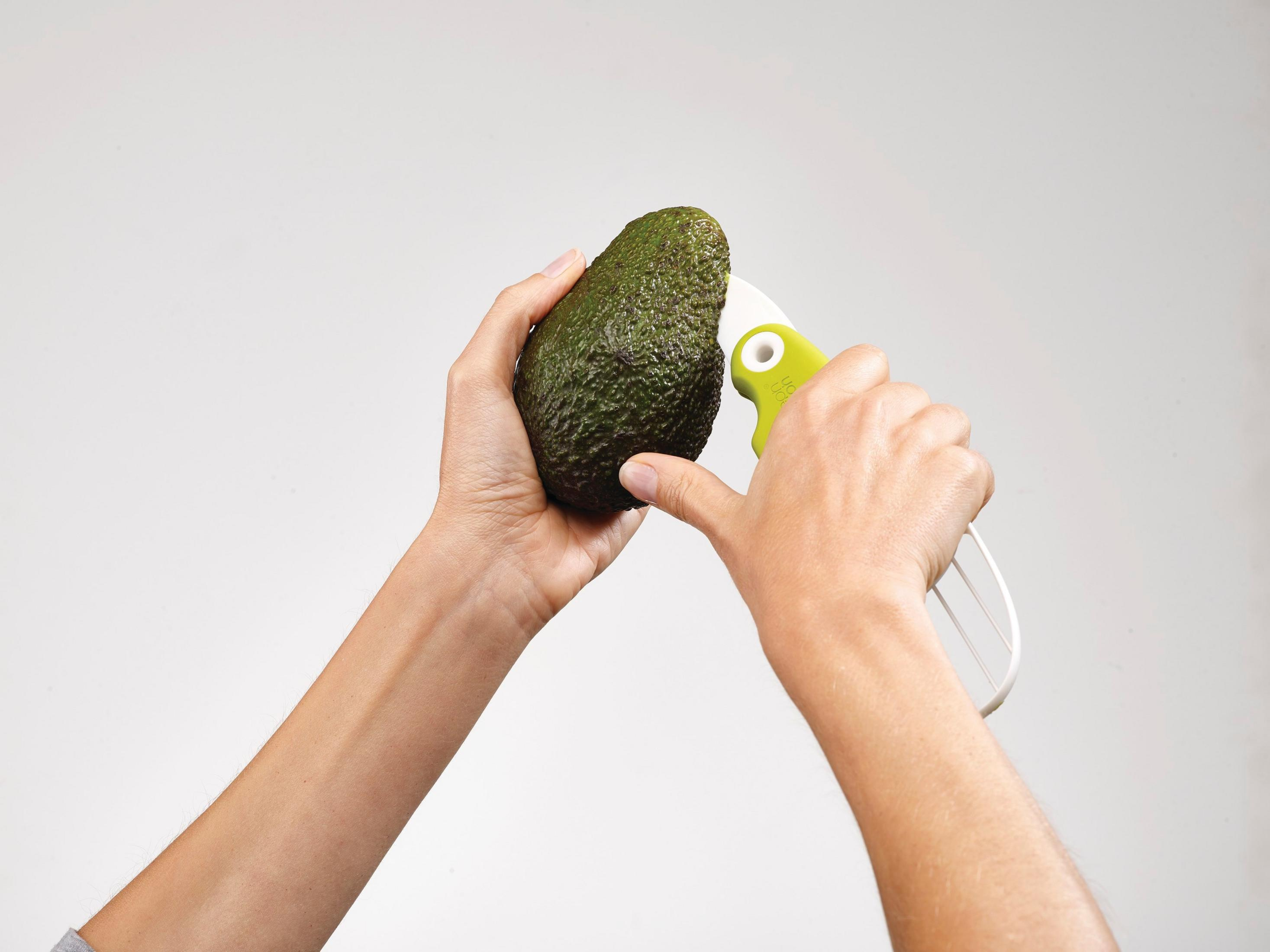 Manos sosteniendo un aguacate y una herramienta para quitar el hueso.