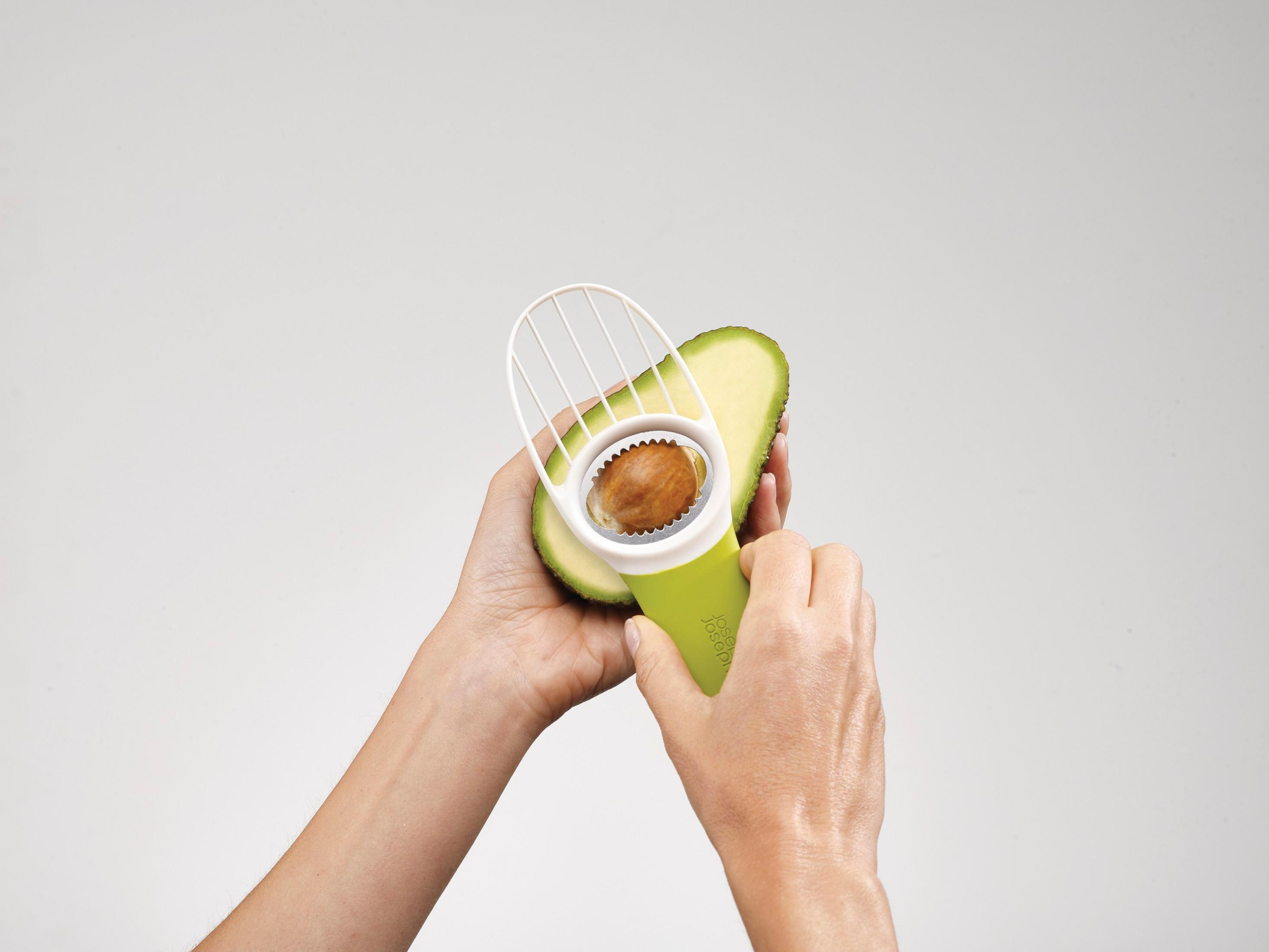 Manos sosteniendo un aguacate y una herramienta para quitar el hueso.
