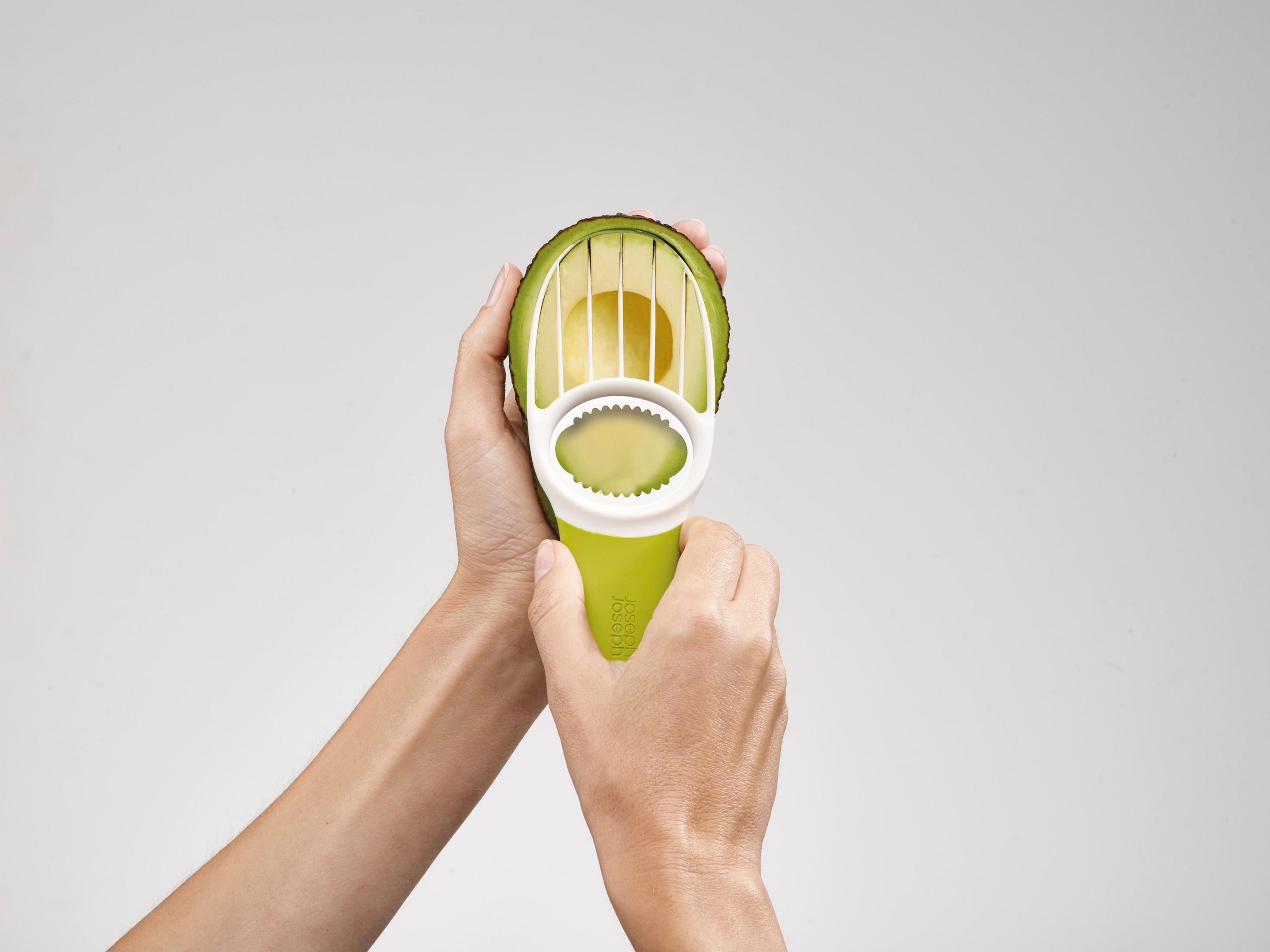 Manos sosteniendo un aguacate que se corta con una herramienta blanca y verde.