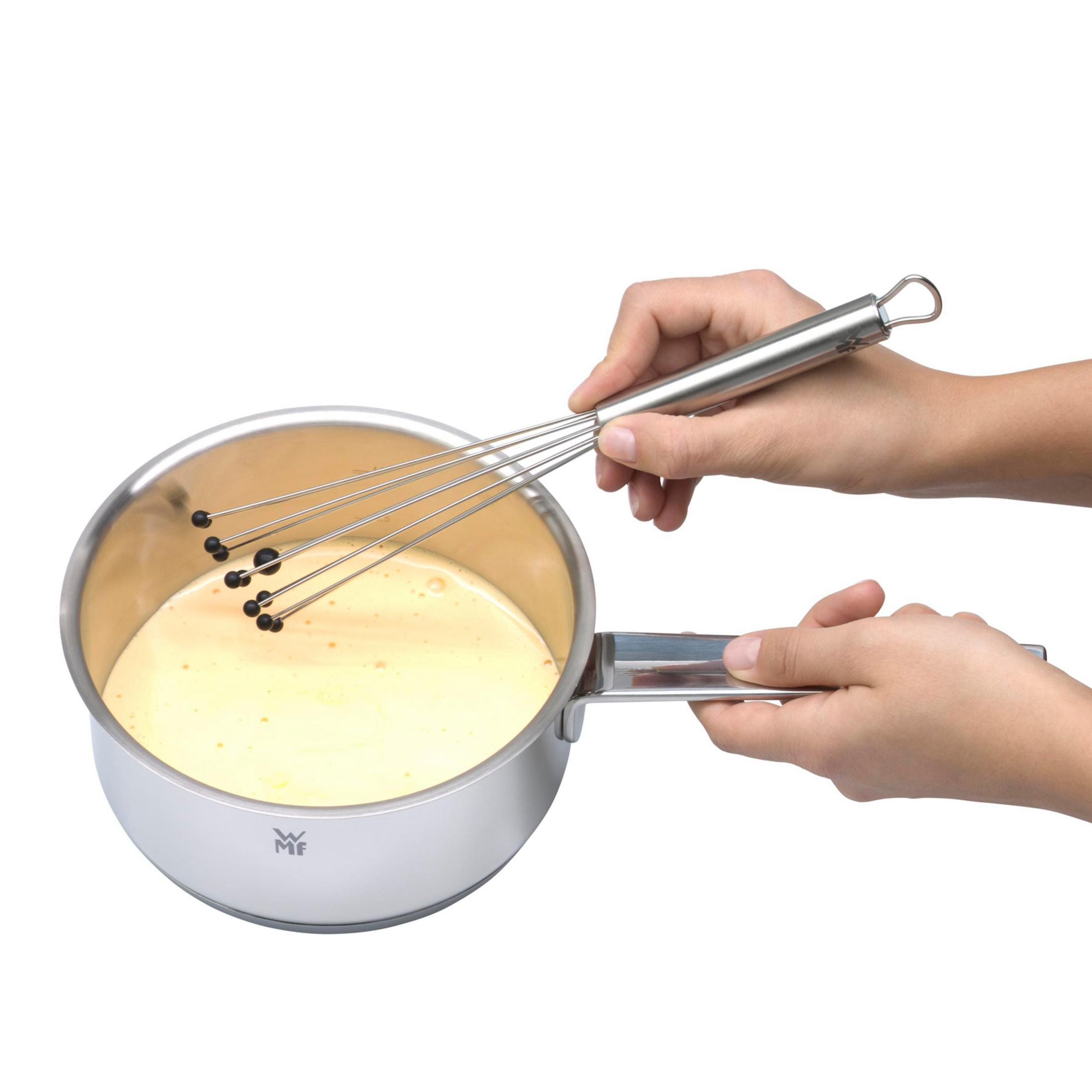 Osoba ubija żółty płyn w garnku ze stali nierdzewnej za pomocą trzepaczki. Garnek ma uchwyt.