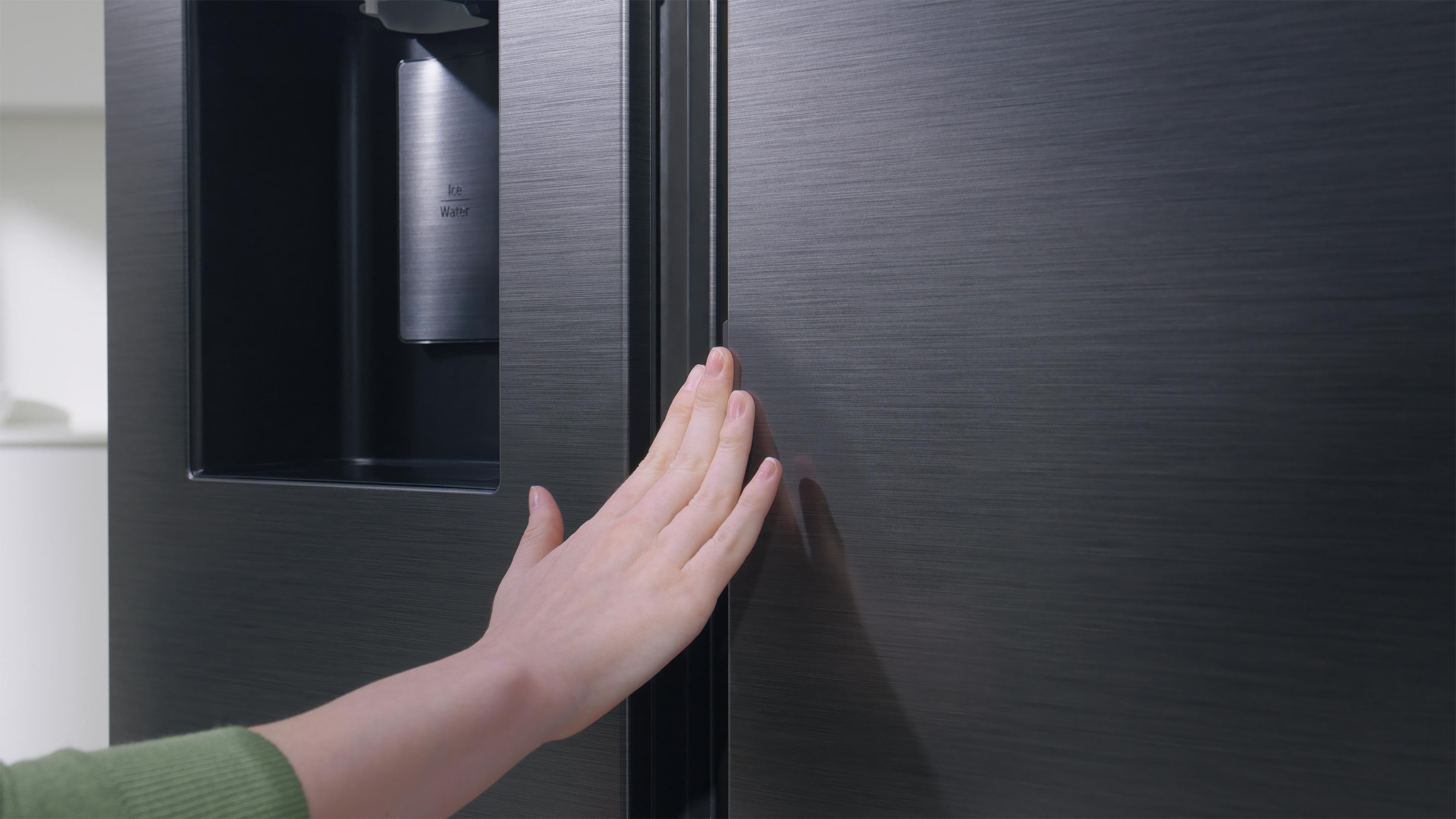 Ręka osoby sięgająca do ciemnych drzwi lodówki z dozownikiem lodu i wody.