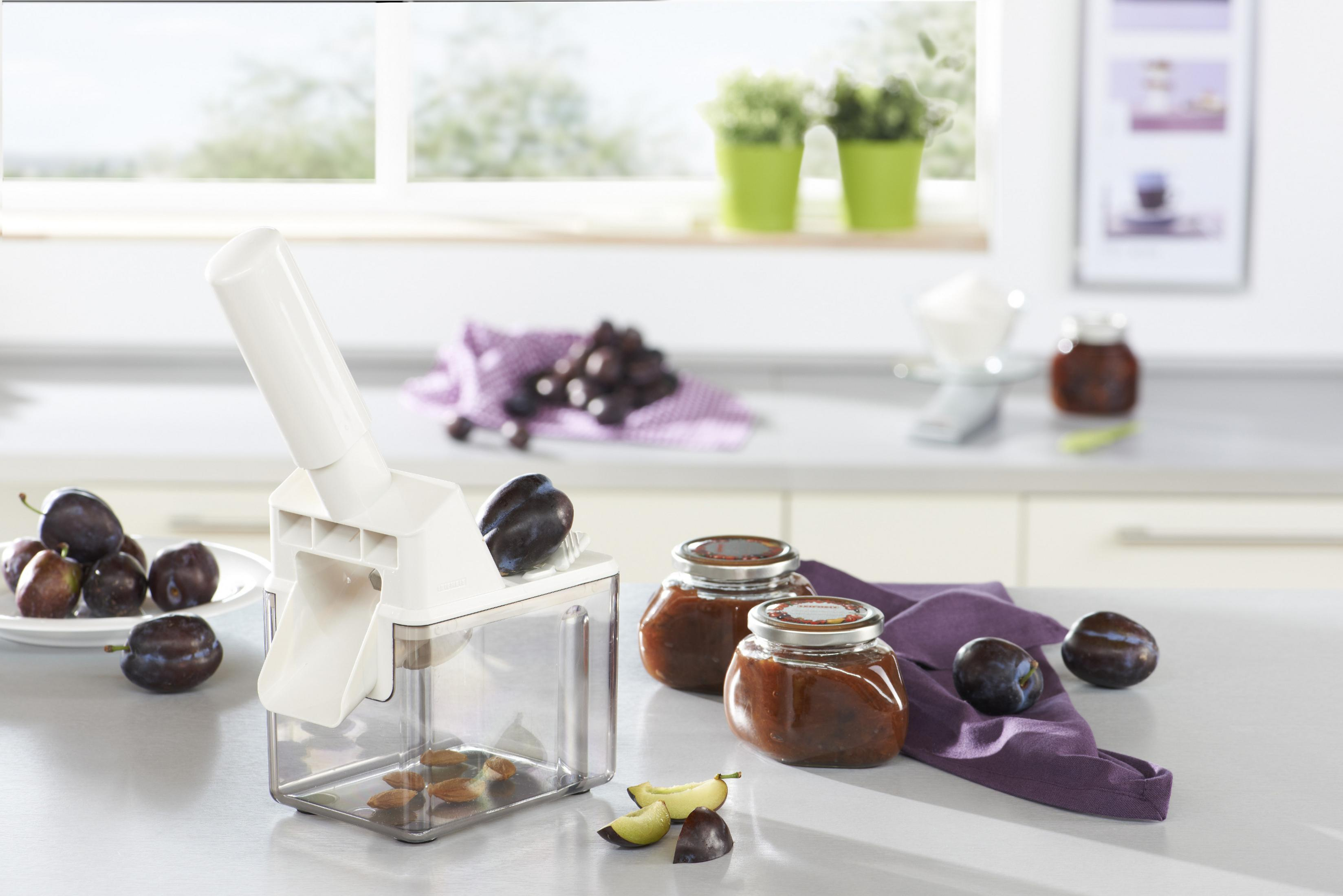 Eine weiße Pflaumenentkernmaschine mit Pflaumen und Marmeladengläsern.
