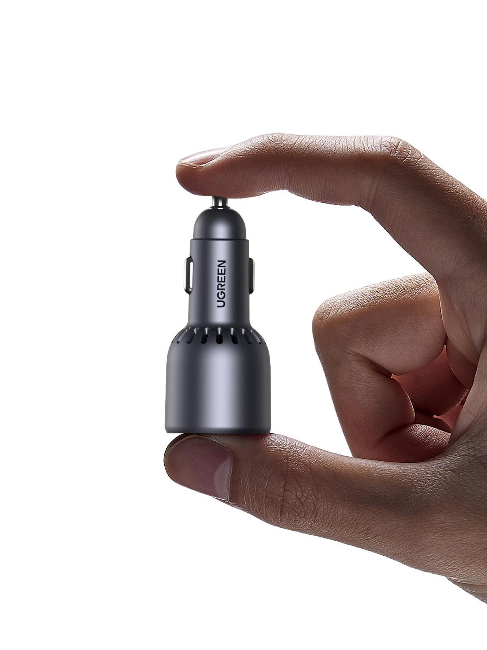 Dłoń trzymająca małą, ciemnoszarą ładowarkę samochodową UGREEN. Białe tło.