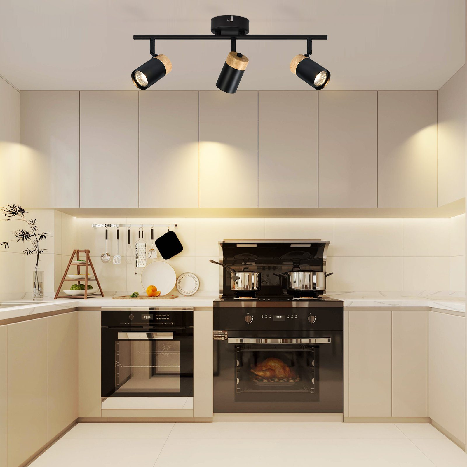 Cucina con tre faretti neri. Colore legno e nero con mobili ed elettrodomestici bianchi.