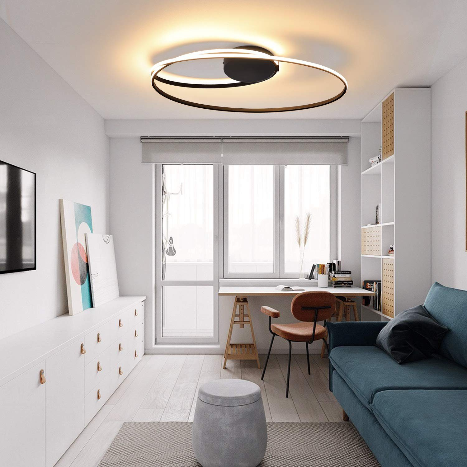Soggiorno moderno con lampada da soffitto circolare, scrivania, divano blu e mobili bianchi.