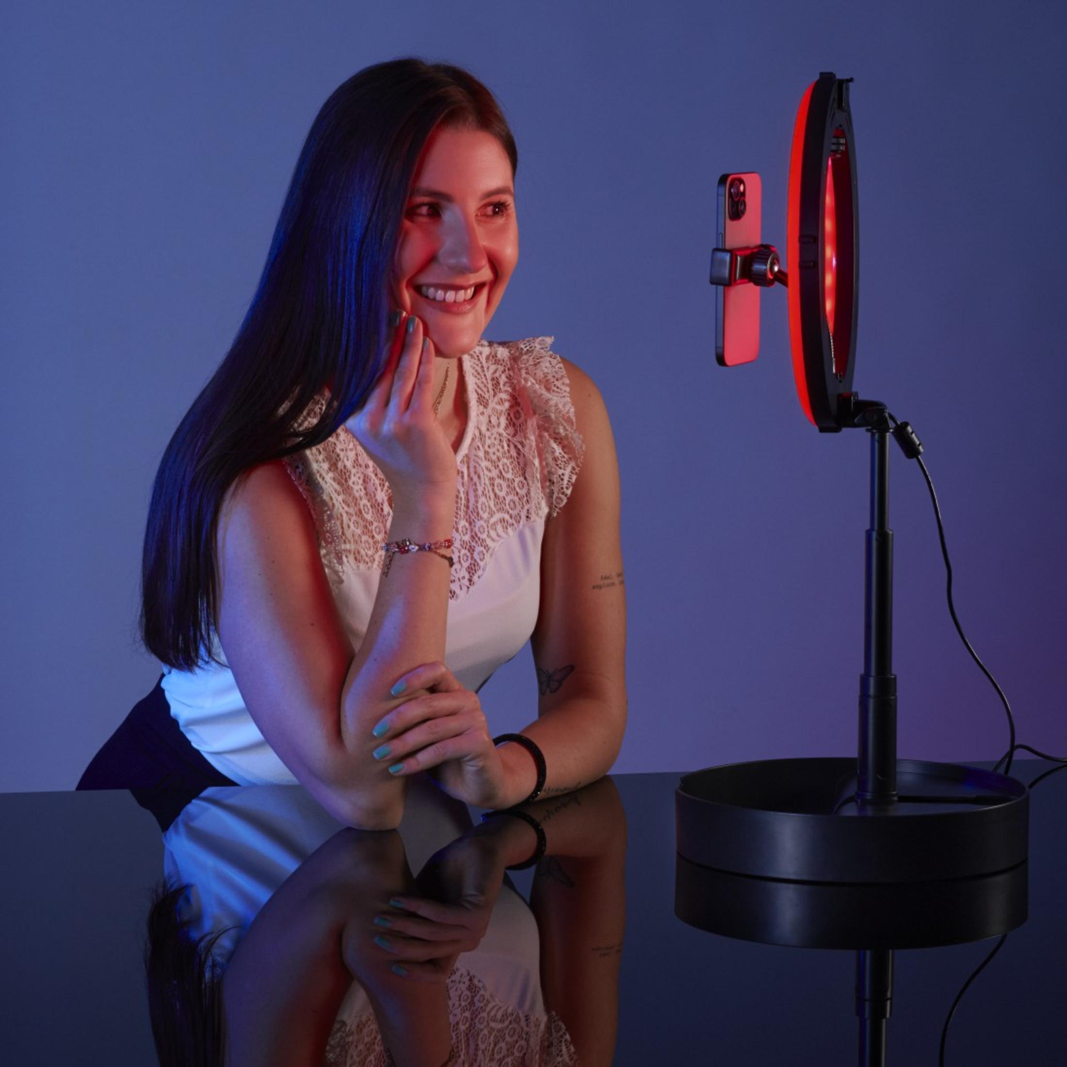 Kobieta używająca lampy pierścieniowej z telefonem, uśmiechnięta do kamery.