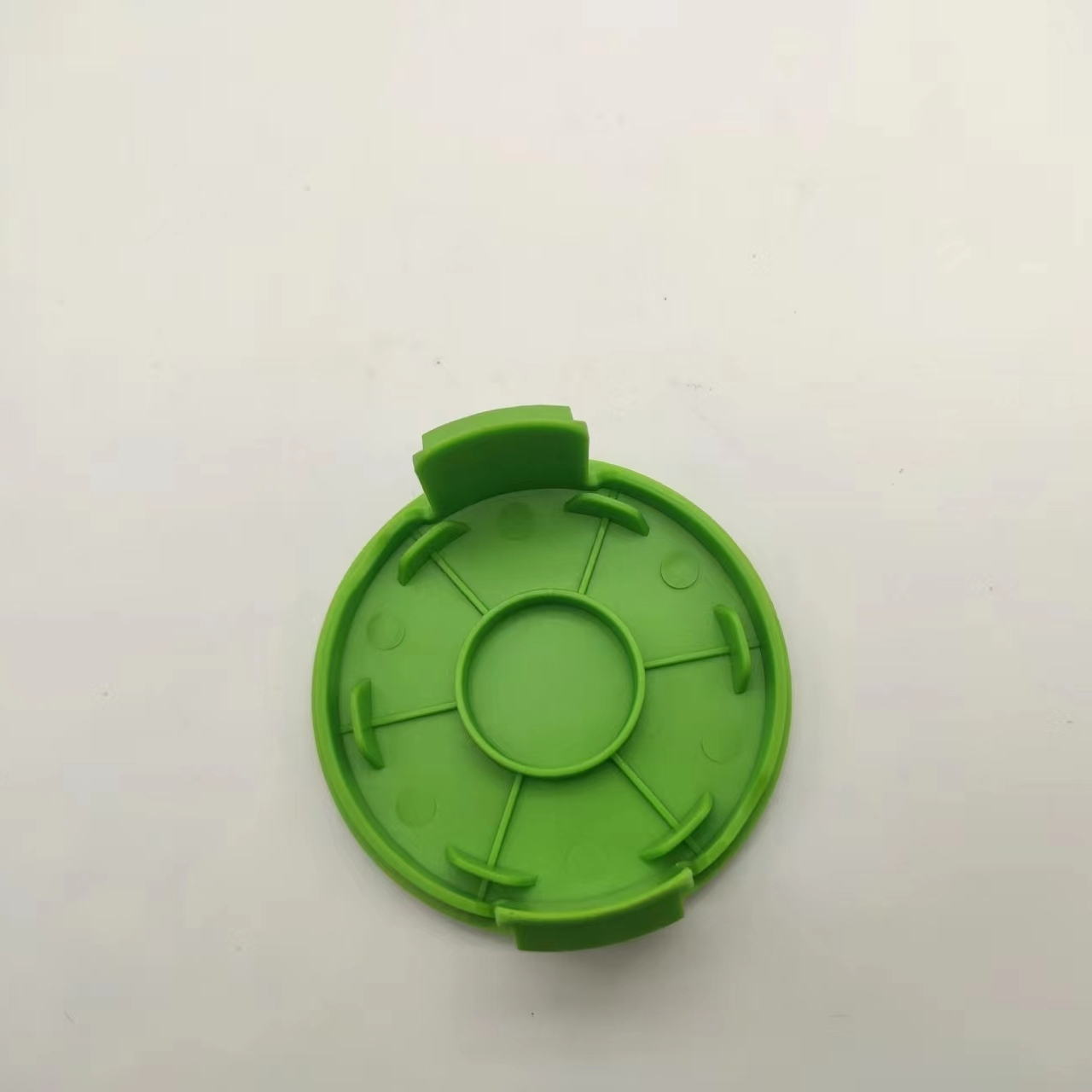 Grüne Fadenschneiderabdeckung, kreisförmig mit einem zentralen Loch und radialen Linien, vor weißem Hintergrund.