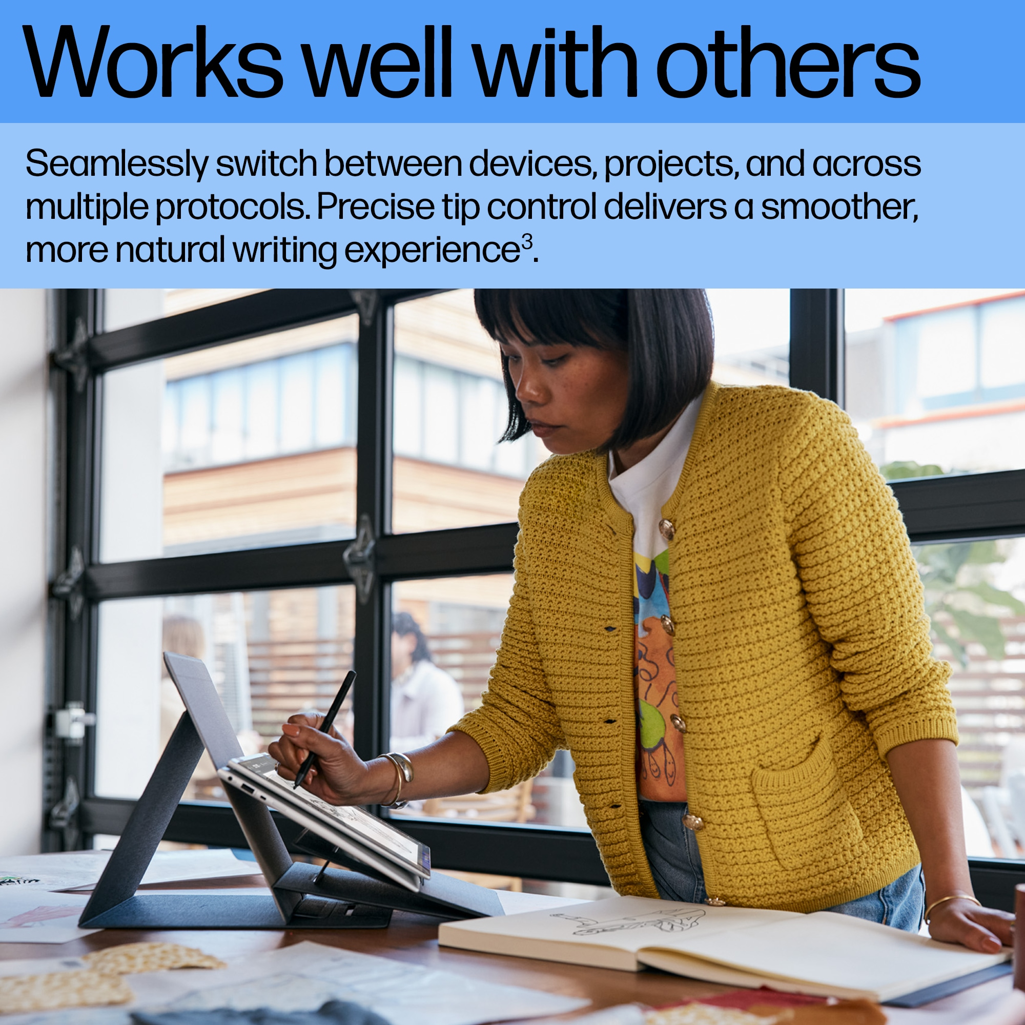 Kobieta używająca pióra na tablecie. Żółta kurtka. Stół i okno w tle.