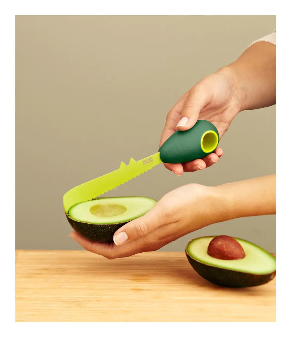 Hände halten eine Avocado und ein grün-gelbes Schneidewerkzeug, mit einem Hintergrund aus Holz.