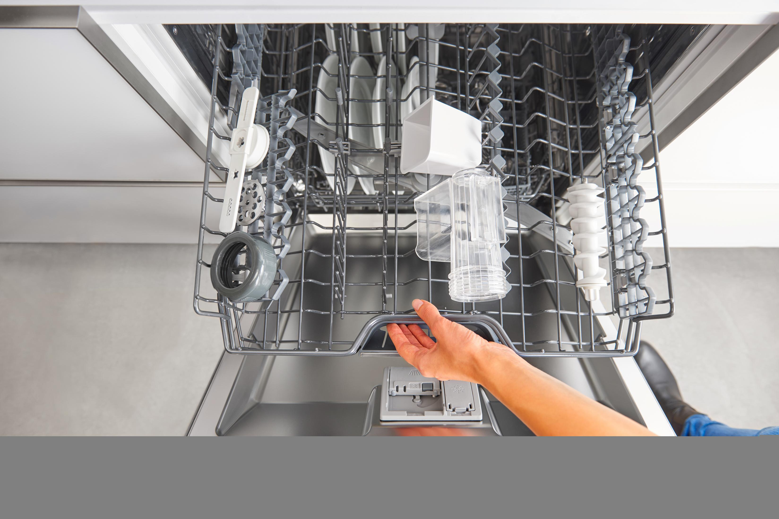 Otwarta zmywarka z naczyniami. Ręka chwyta za uchwyt szuflady.