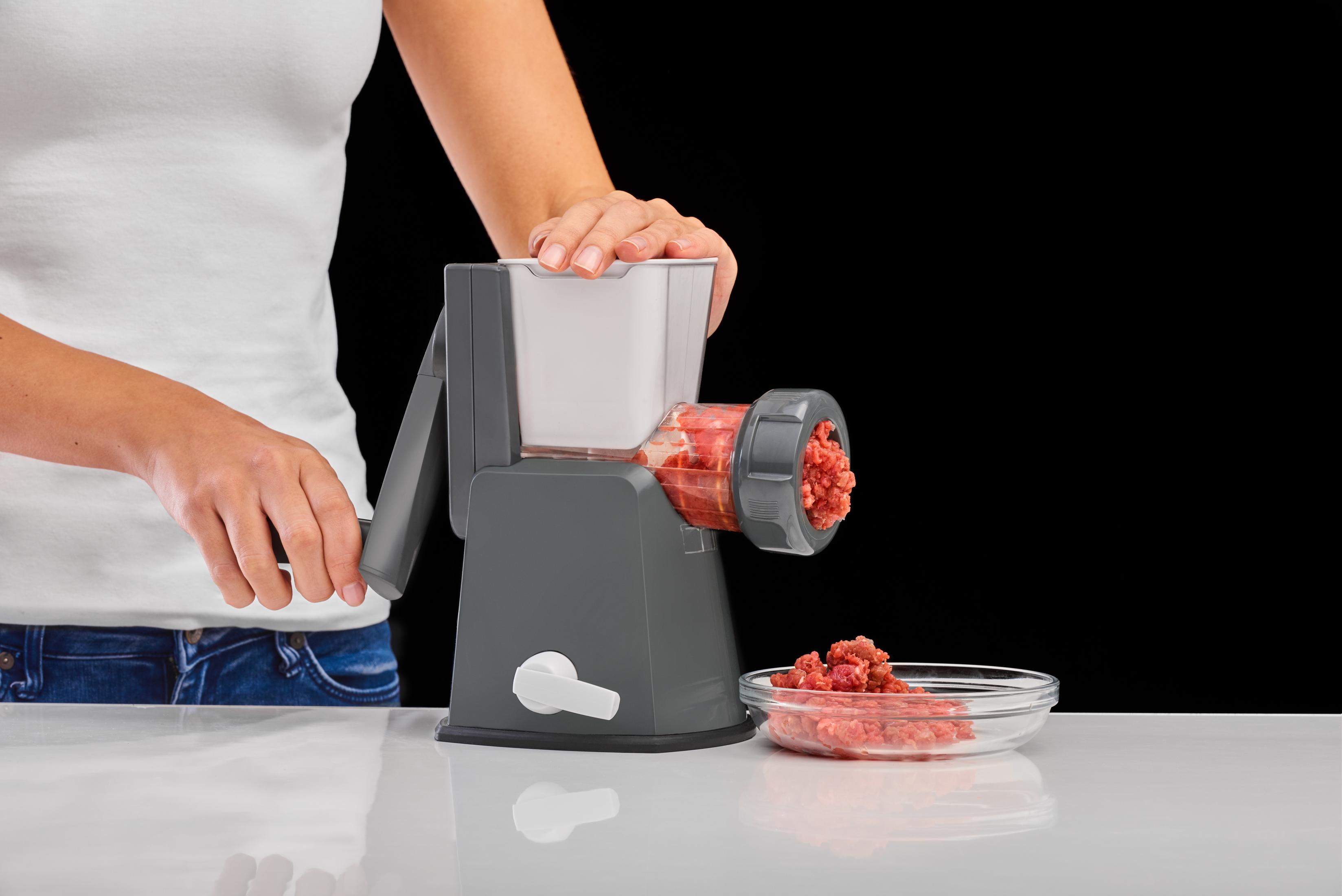 Ręce używają szarej maszynki do mięsa. Mielone trafia do miski.