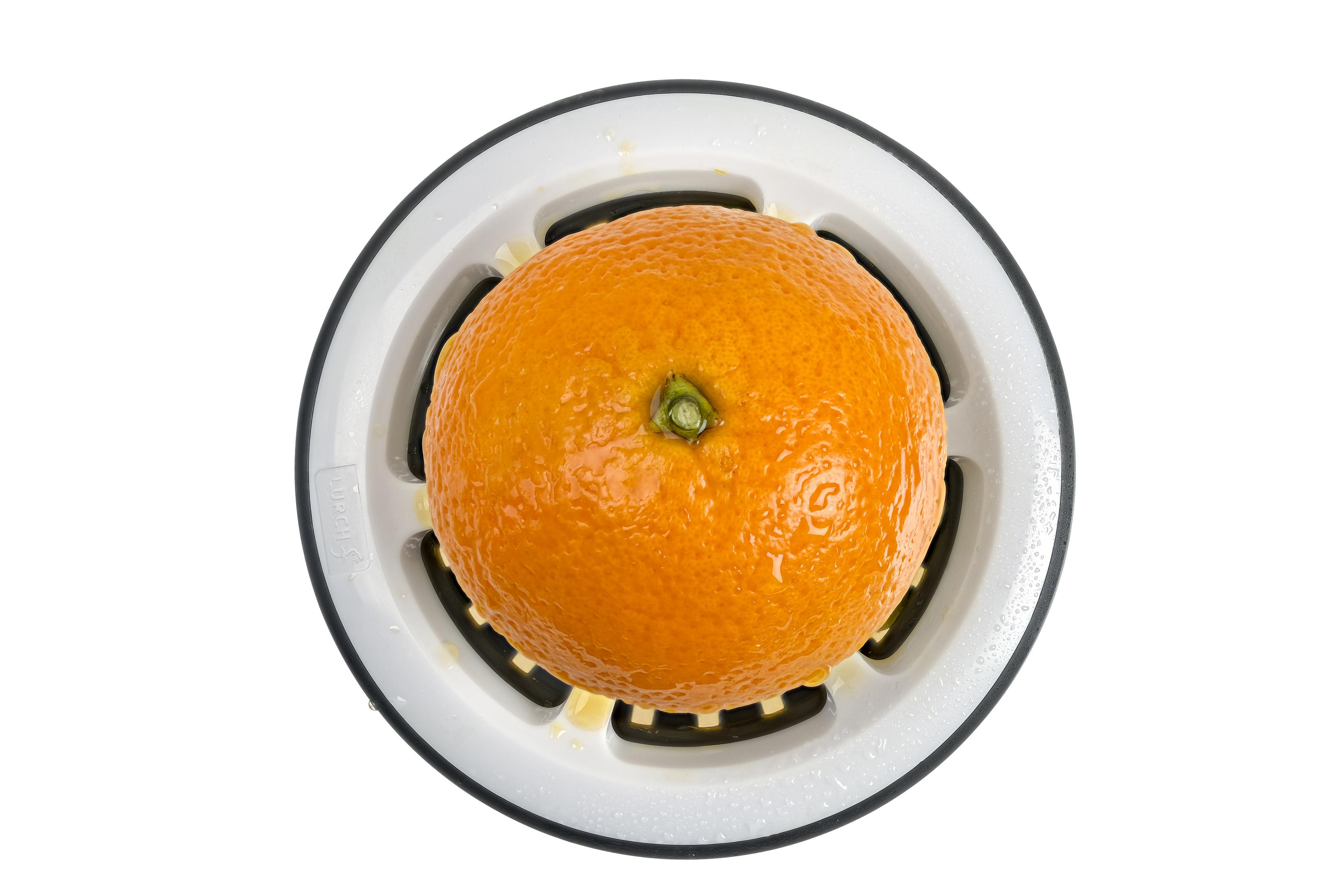 Eine Orange in einem weiß-schwarzen Entsafter, von oben fotografiert.