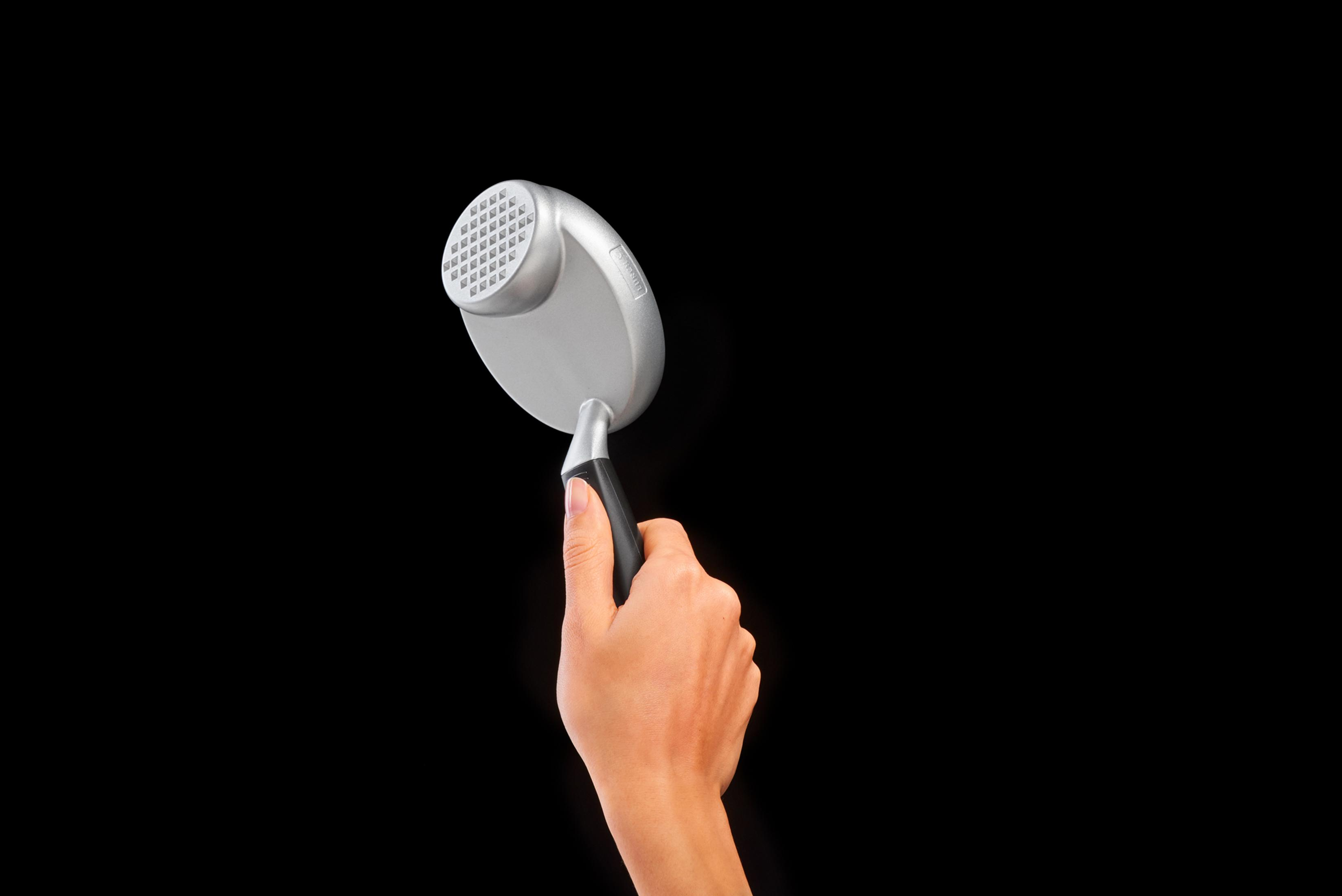 Eine Hand hält ein silbernes Kopfmassagegerät vor schwarzem Hintergrund.