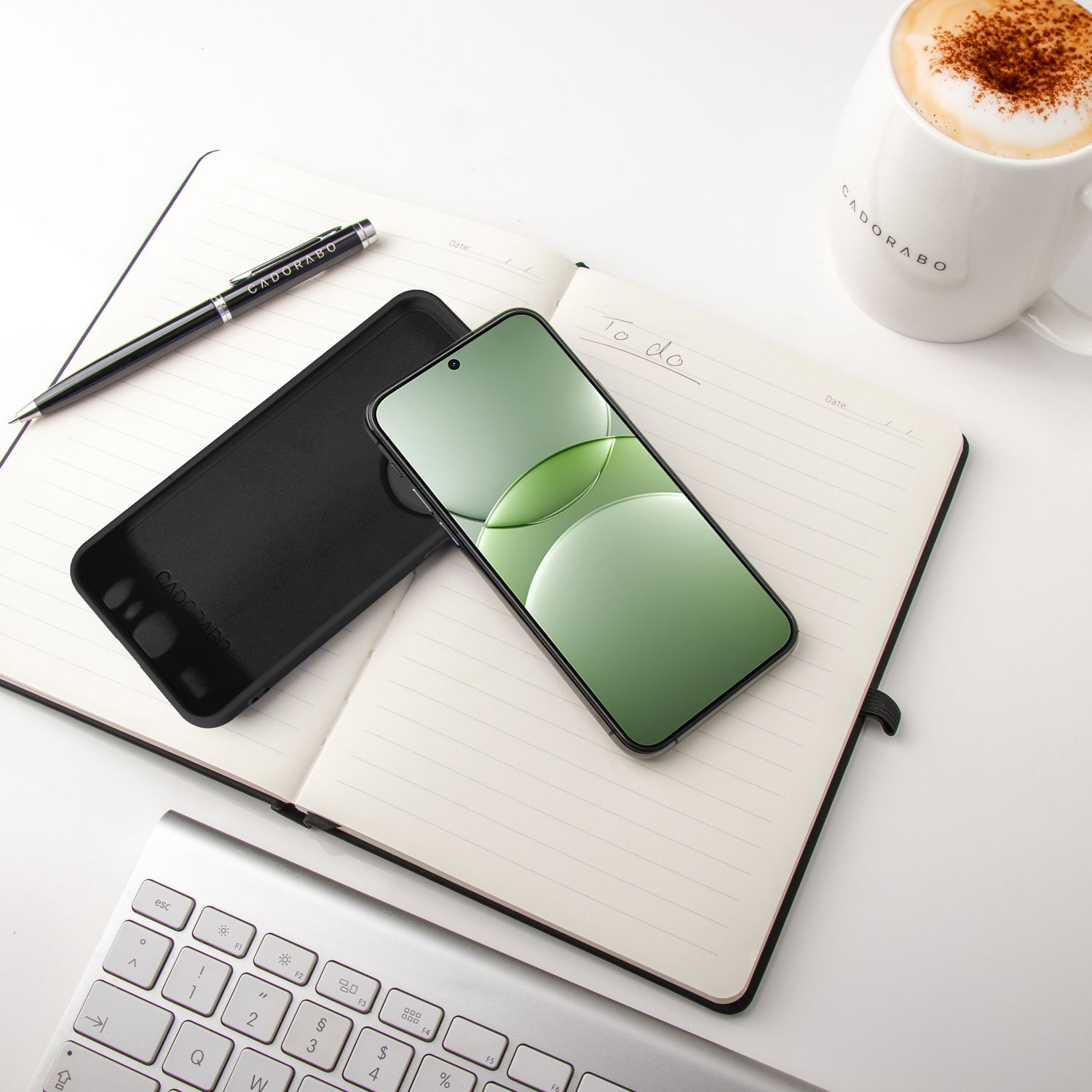 Smartphone und Notizbuch auf einem weißen Tisch. Auch ein Stift und eine Tasse Latte.