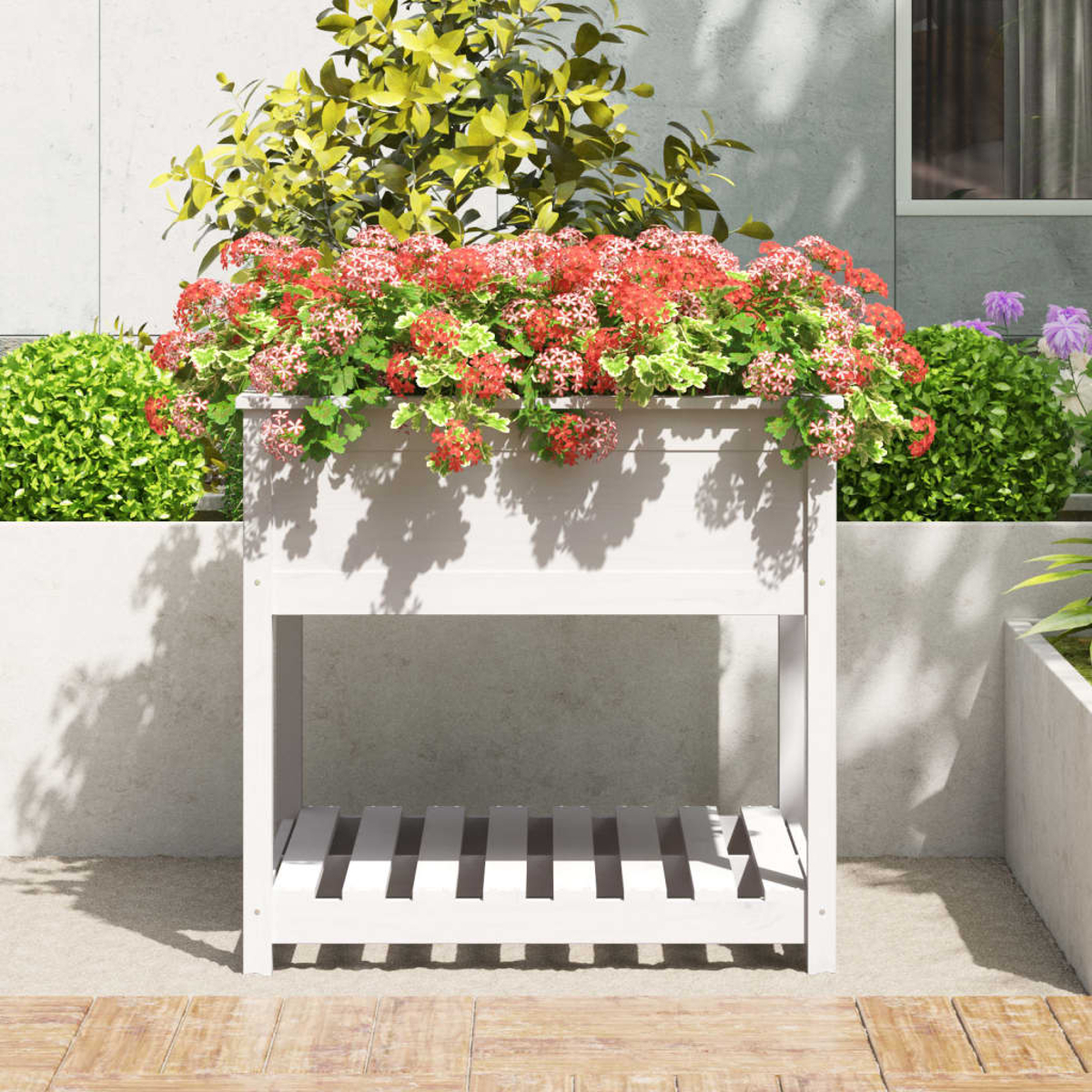 Weißes Hochbeet mit Blumen. Es steht auf einer Terrasse mit Wand und Zaun im Hintergrund.