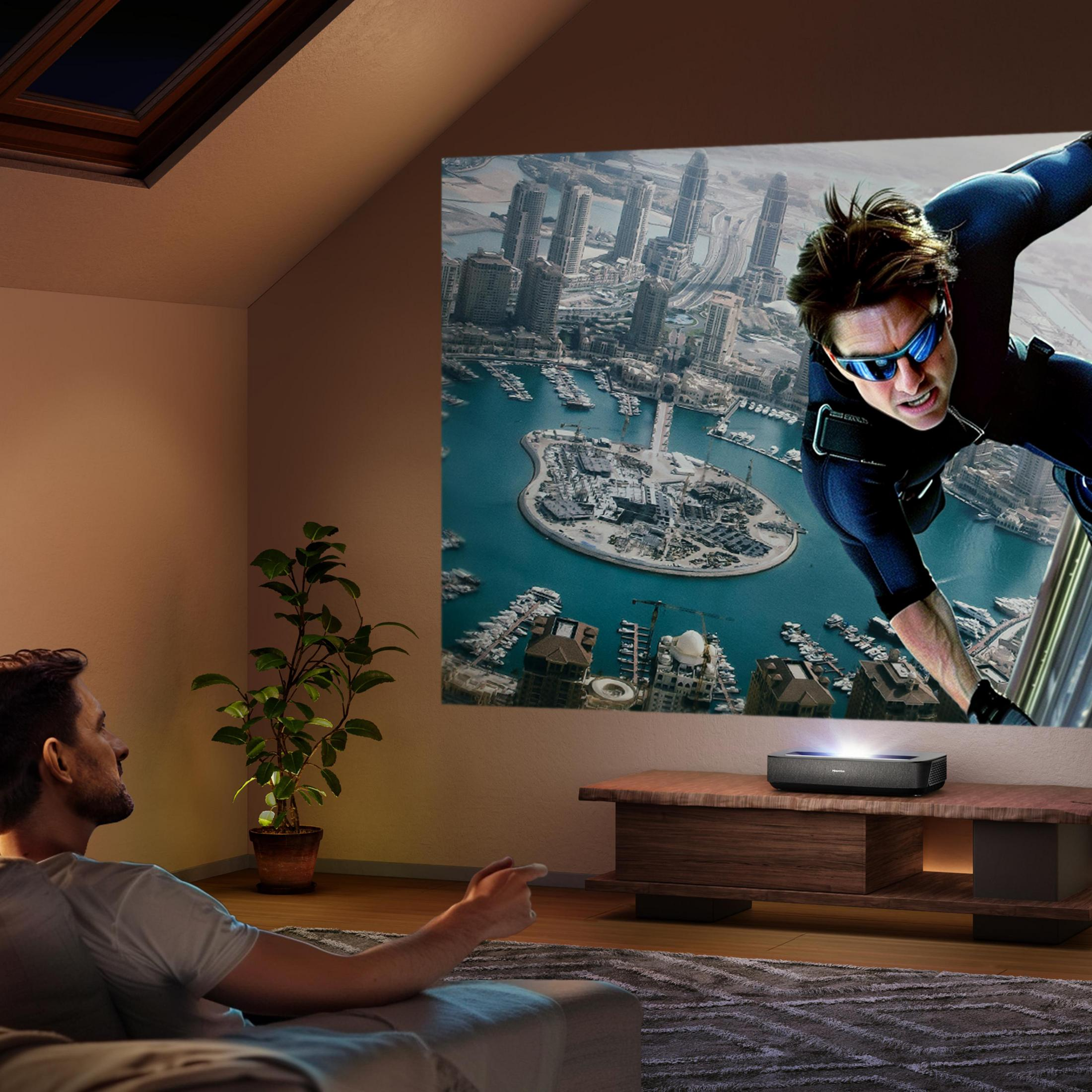 Mężczyzna ogląda film wyświetlany na ścianie. Na ekranie Tom Cruise.