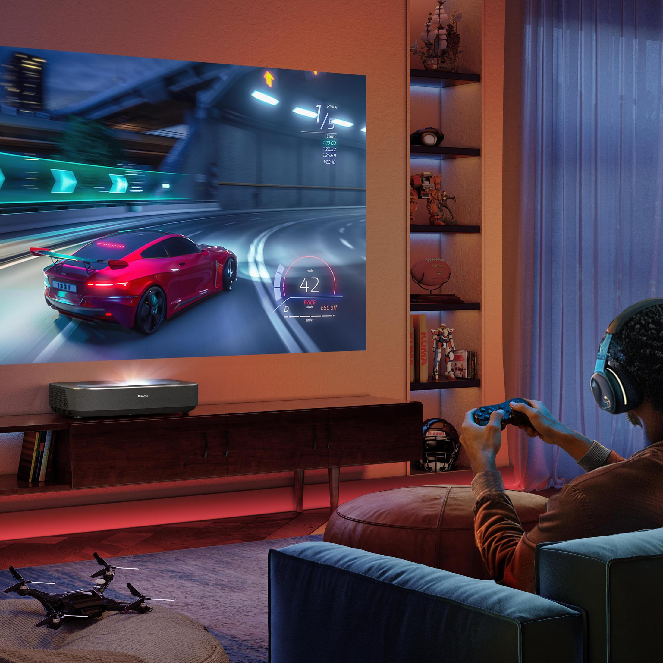 Mężczyzna gra w grę wyścigową na rzutowanym ekranie. Dron na stole. Czerwony samochód, 42 mph.