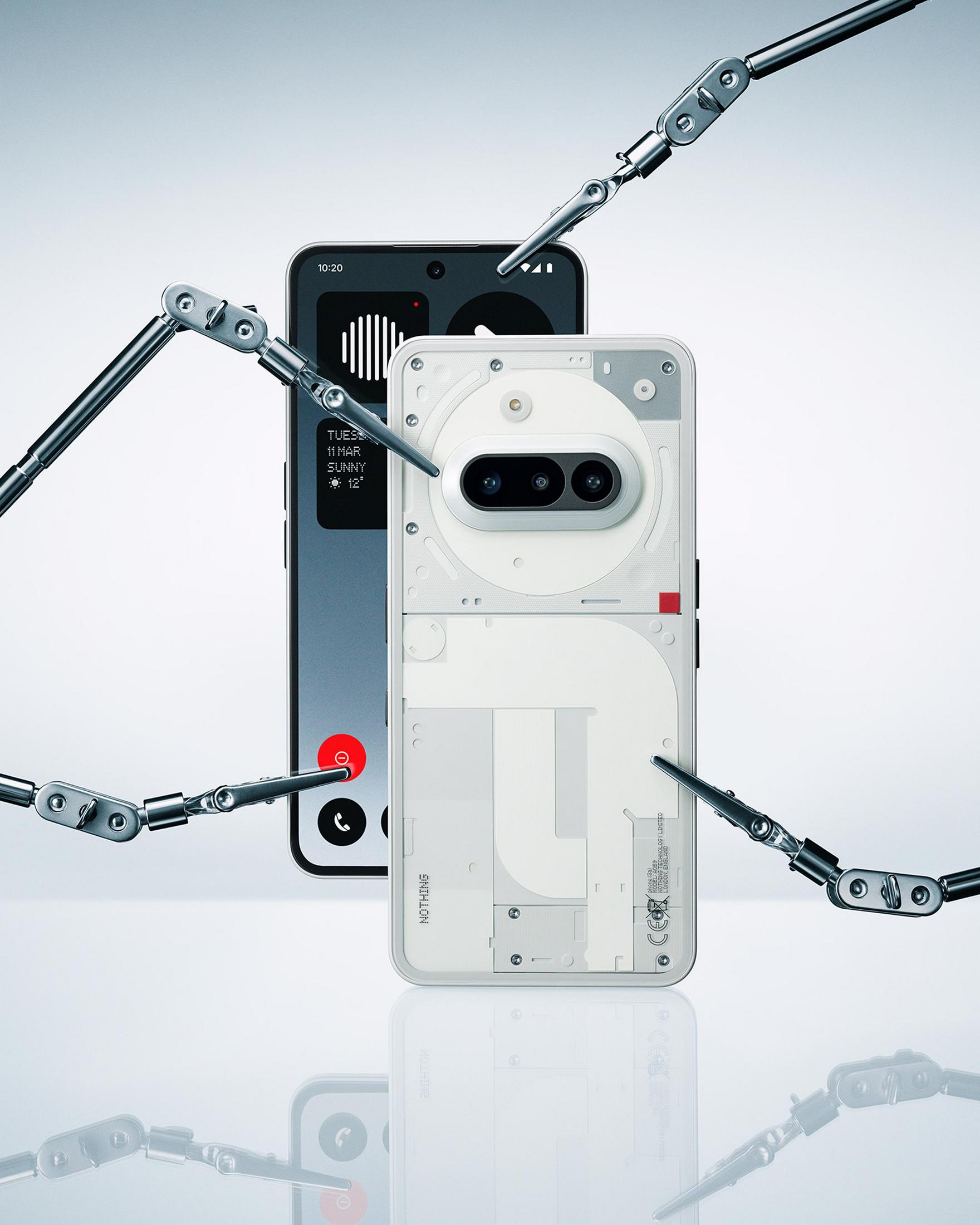 Dwa smartfony, czarny i biały z przezroczystym tyłem. Otaczają je mechaniczne ramiona.