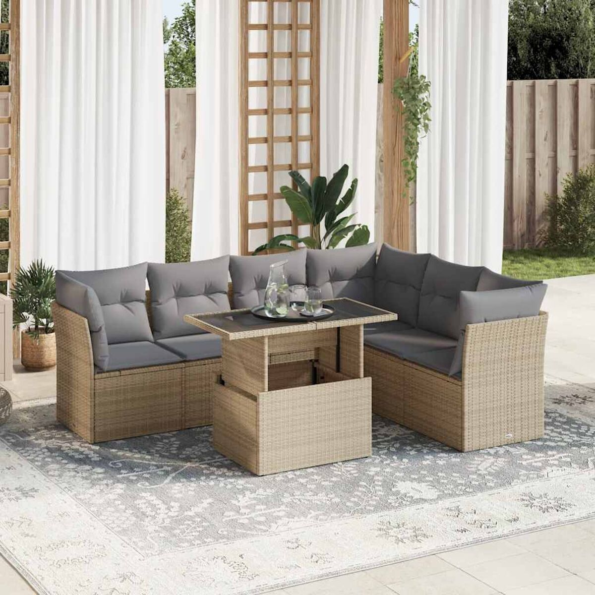 Divano angolare da esterno in rattan beige con cuscini grigi. Tavolo con vetro e brocca.