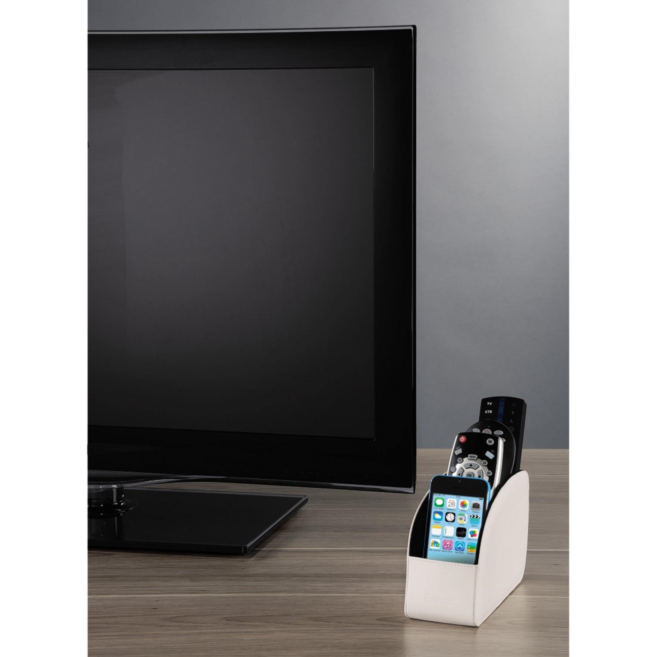 Ein Fernseher steht auf einem Holzschreibtisch. Es gibt ein Telefon und Fernbedienungen in einem Halter. Grauer Hintergrund.