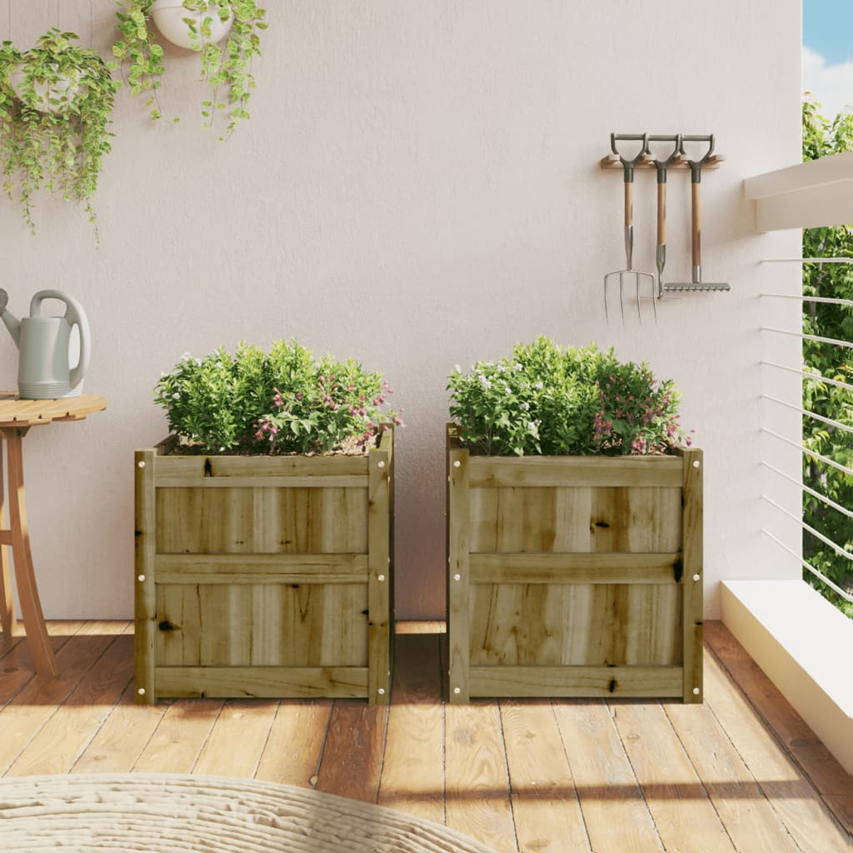 Zwei Holzpflanzkästen auf einem Balkon mit Pflanzen. Grüne Pflanzen mit rosa Blüten. Weißer Wandhintergrund.