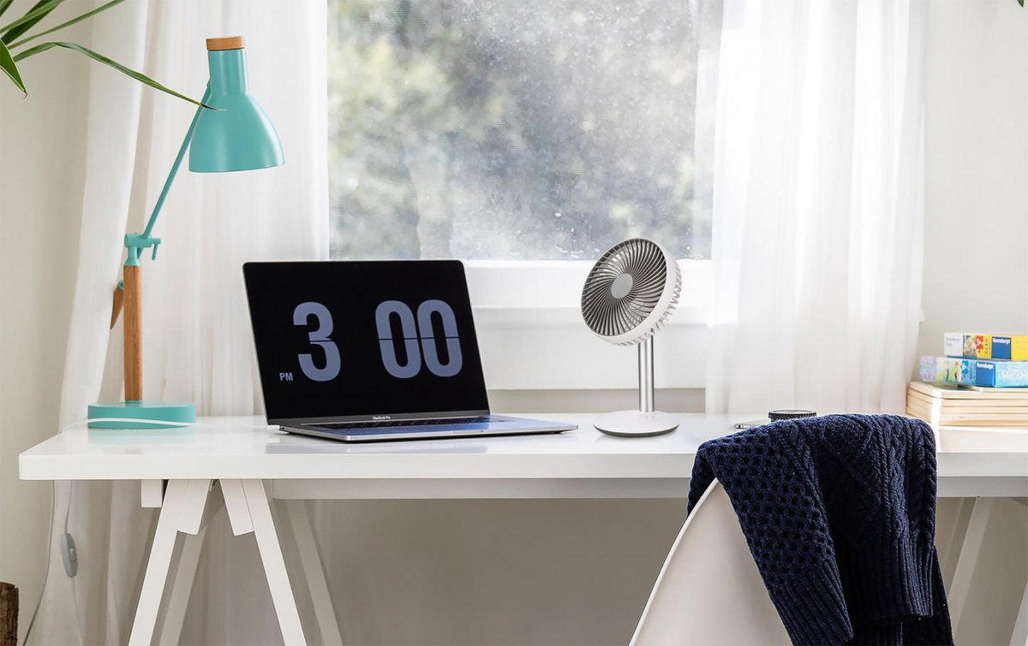 Schreibtisch mit Laptop um 15:00 Uhr, Lampe, Ventilator und Fenster.
