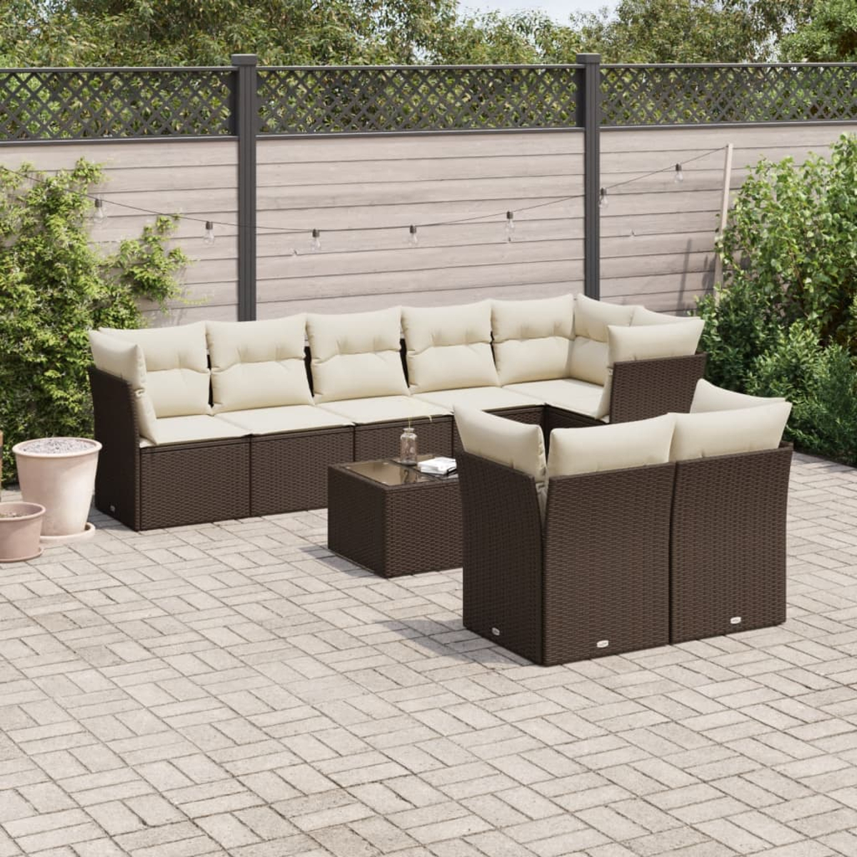 Patio all'aperto. Mobili marroni intrecciati con cuscini beige. Patio in pietra con piante sullo sfondo.
