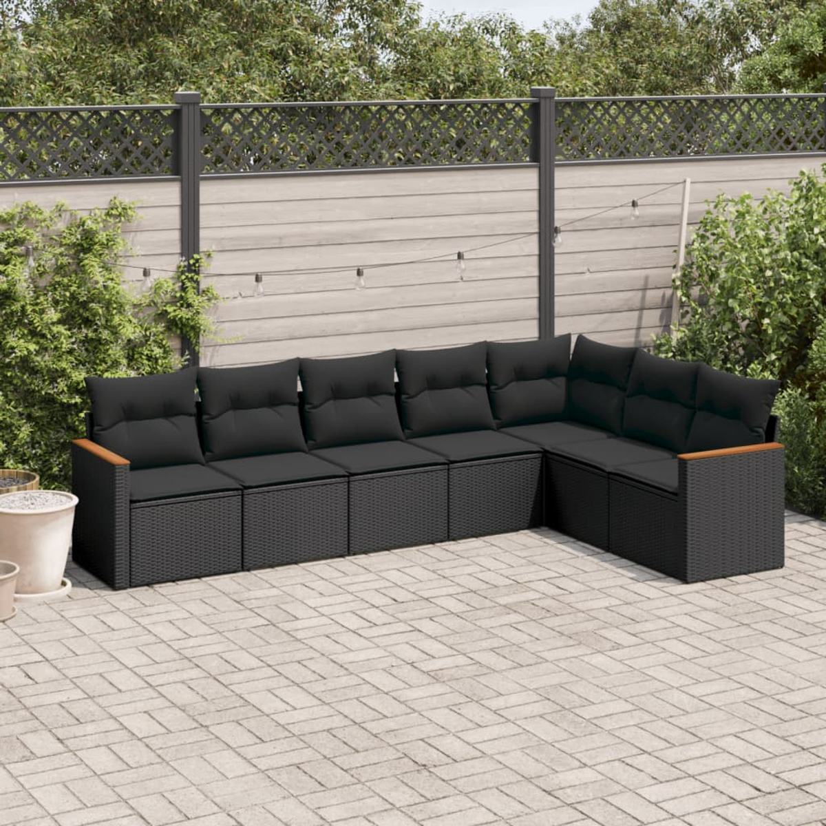 Schwarzes geflochtenes Ecksofa mit schwarzen Kissen in einem Hinterhof mit Zaun.