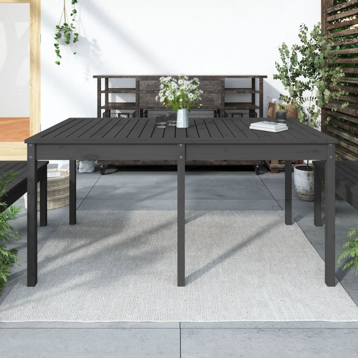 Holztisch im Freien. Der Tisch ist dunkel, mit einer Blumenvase. Auf einem Teppich platziert.