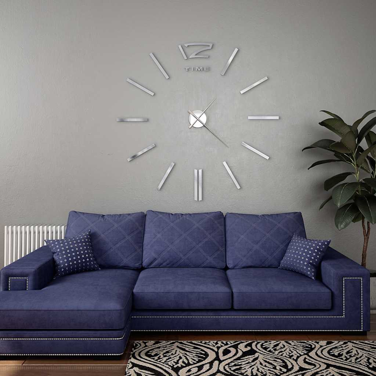 Eine große Uhr und ein blaues Sofa in einem Raum mit grauer Wand und Pflanze.