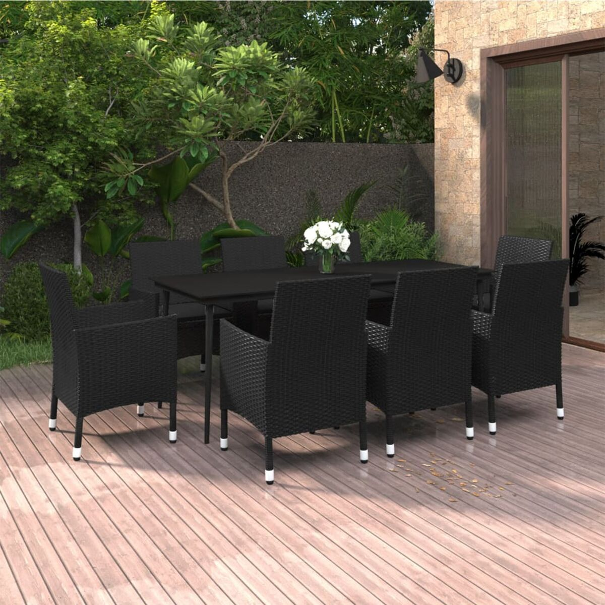 Schwarze Korbstühle und ein Tisch auf einer Holzterrasse mit Blumengesteck im Garten.