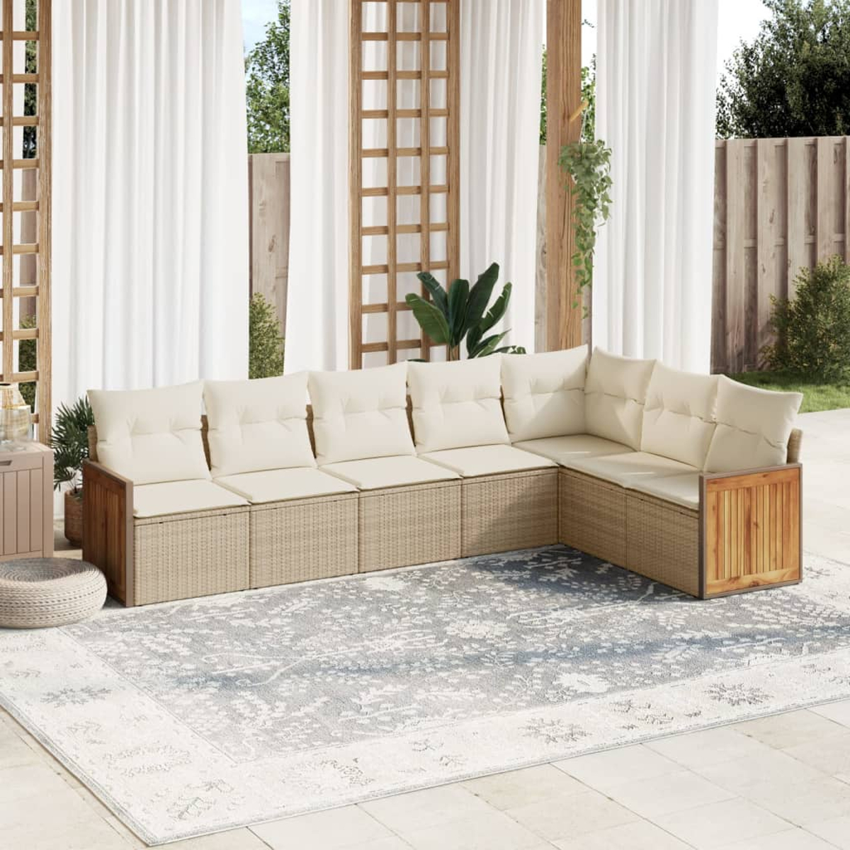 Beiges Rattansofa mit cremefarbenen Kissen, vor Holzzaun und Vorhängen.