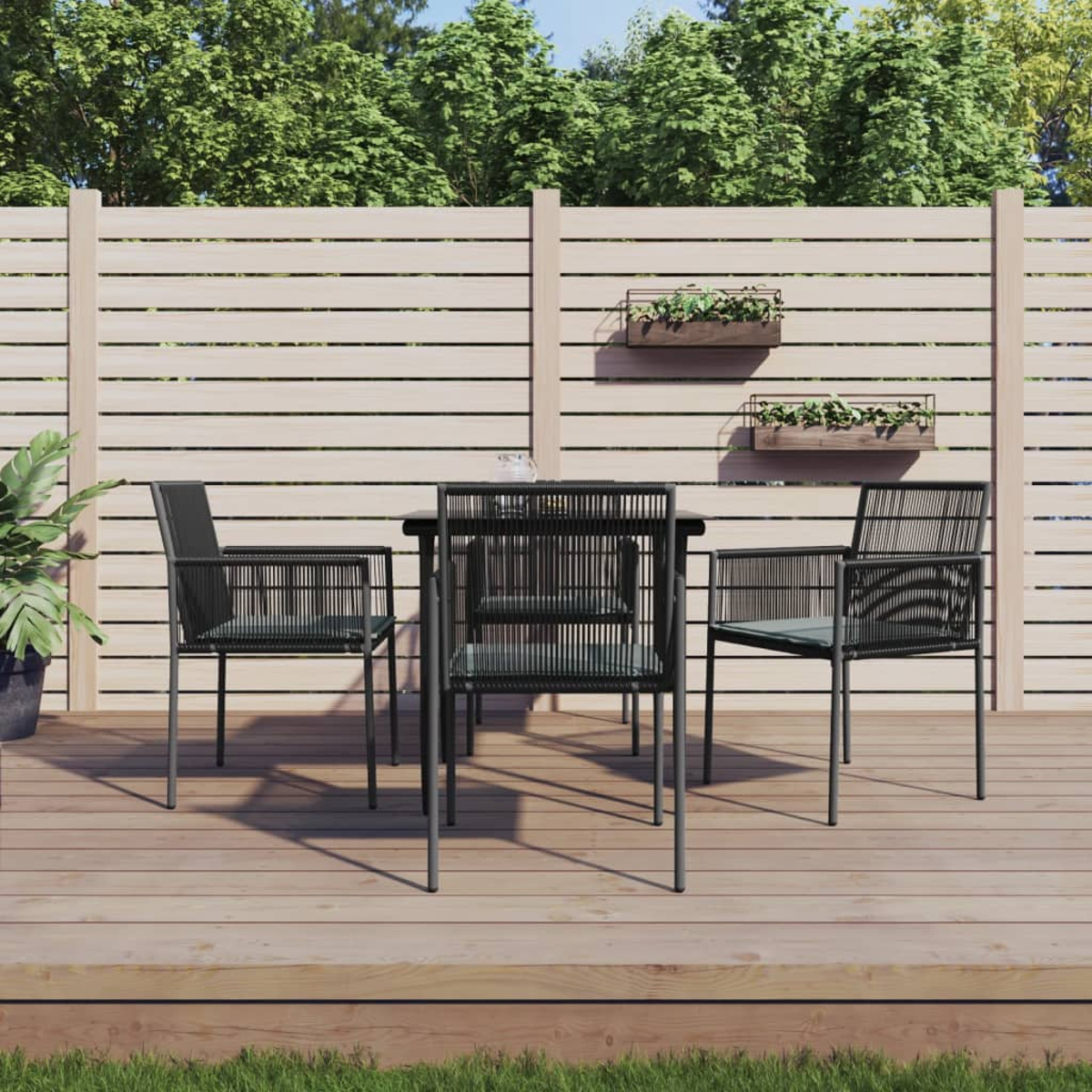 Terrassenset. Vier Stühle um einen Tisch auf einem Deck. Bäume und ein Zaun sind im Hintergrund.