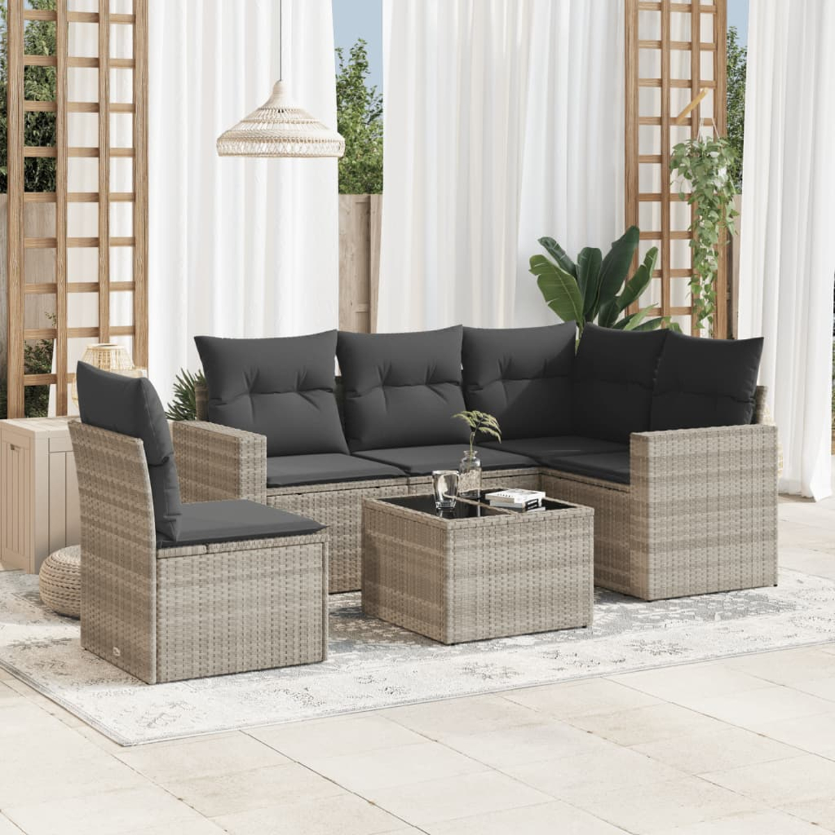 Ein graues Outdoor-Sofa-Set. Es befindet sich auf einer Terrasse mit einem Tisch und Pflanzen. Im Hintergrund ist ein Zaun.
