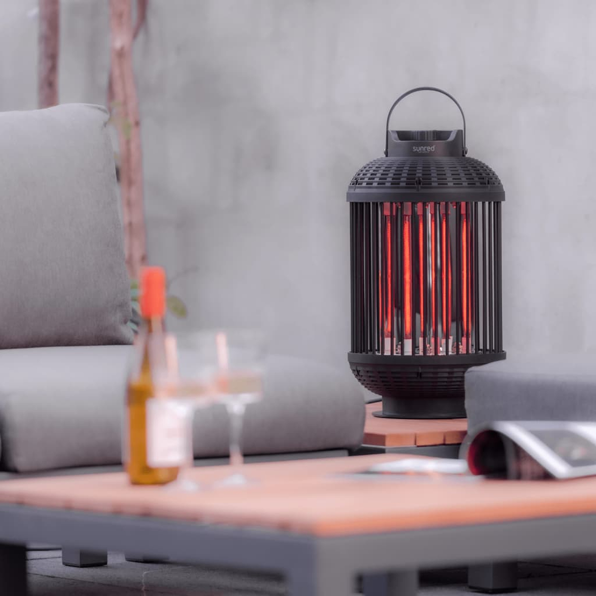 Un radiateur extérieur noir avec des éléments chauffants rouges, avec des verres et une bouteille sur une table.