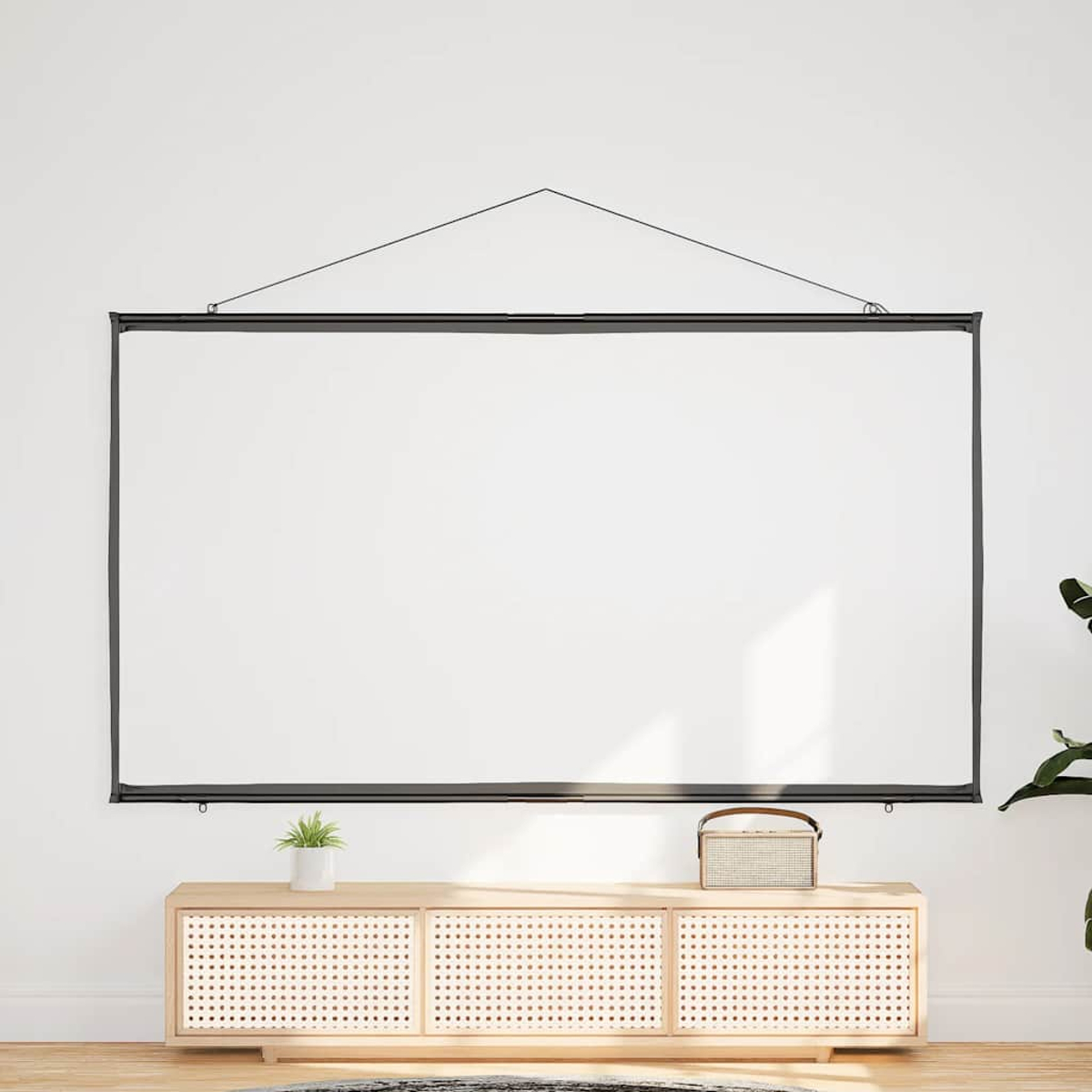 Eine weiße Projektorleinwand hängt. Holzschrank und Pflanze darunter. Weiße Wand.