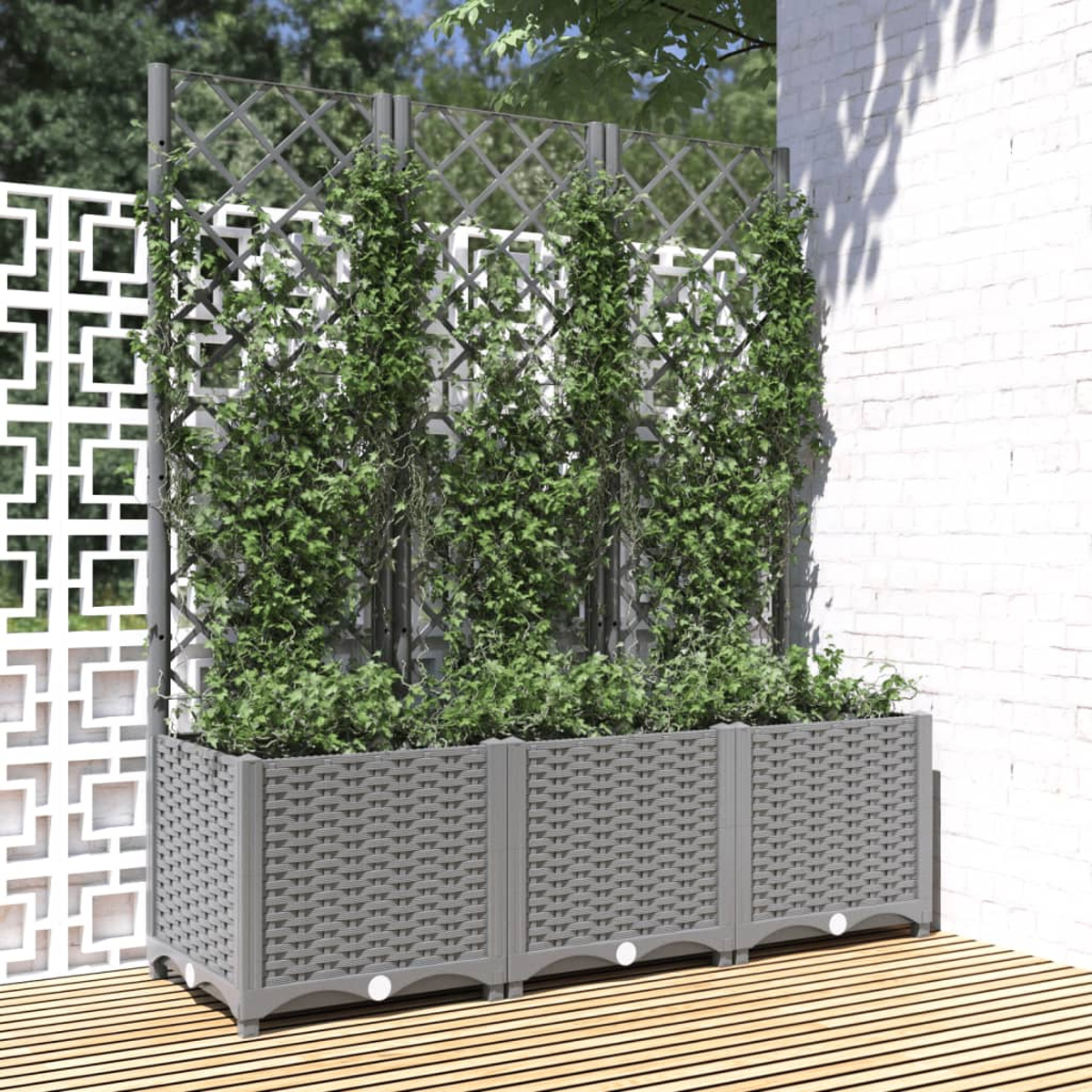 Grauer Pflanzkasten mit grünen Pflanzen und Spalier vor einer weißen Wand und Holzterrasse.