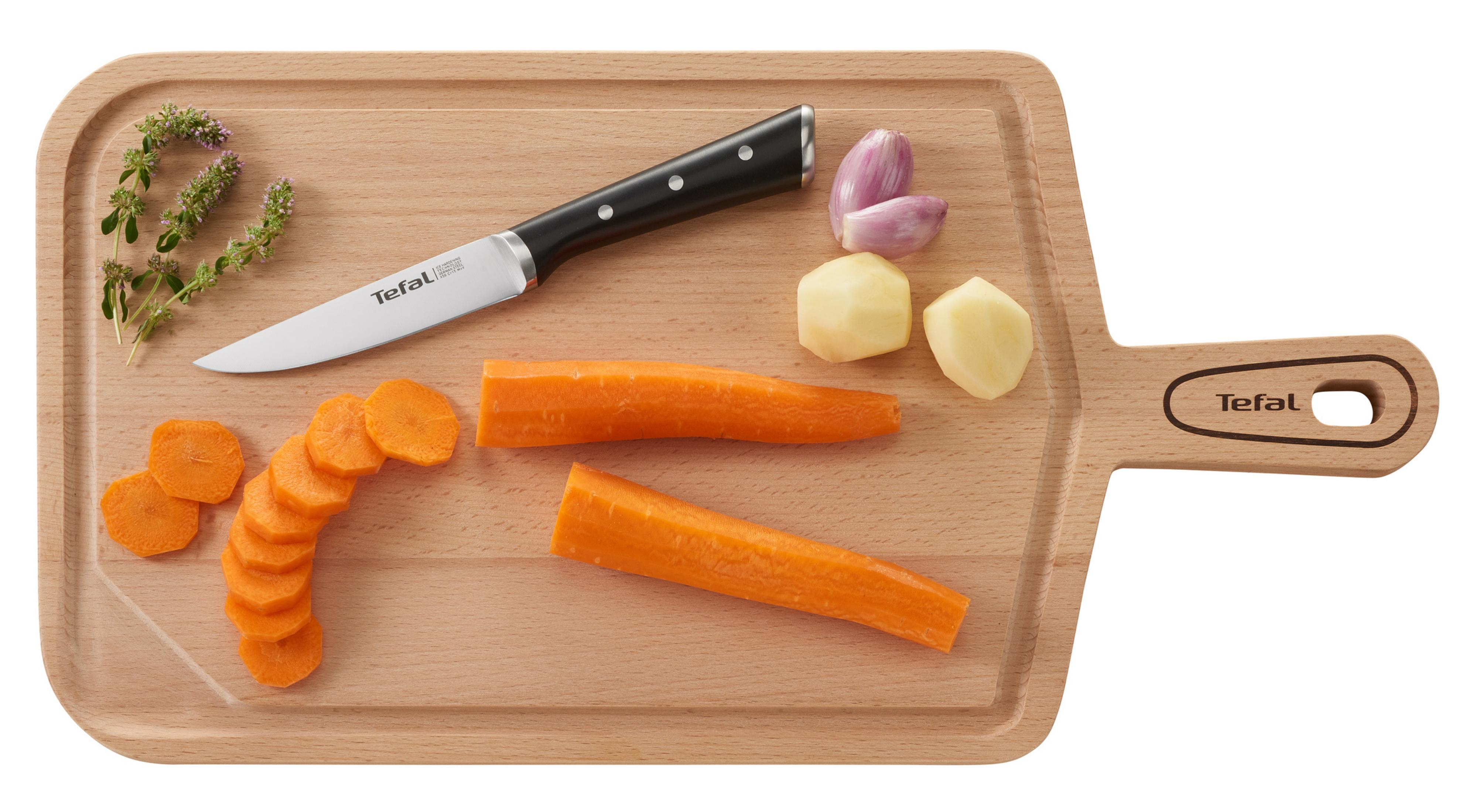 Ein Holzschneidebrett mit Messer, geschnittenen Karotten, Knoblauch, Kartoffeln und Kräutern.