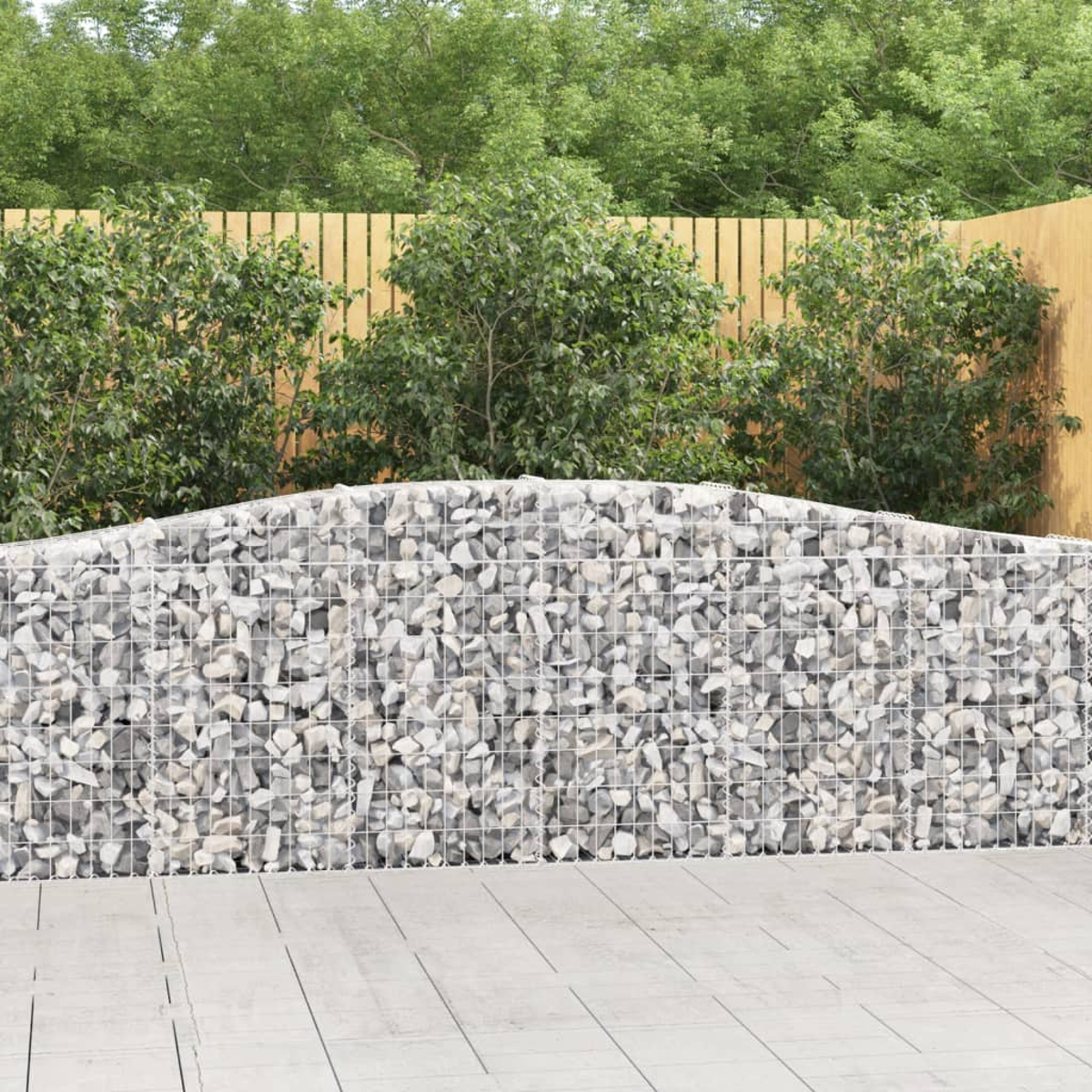 Eine Gabionenwand mit Steinen gefüllt, mit grünen Büschen und Holzzaun.