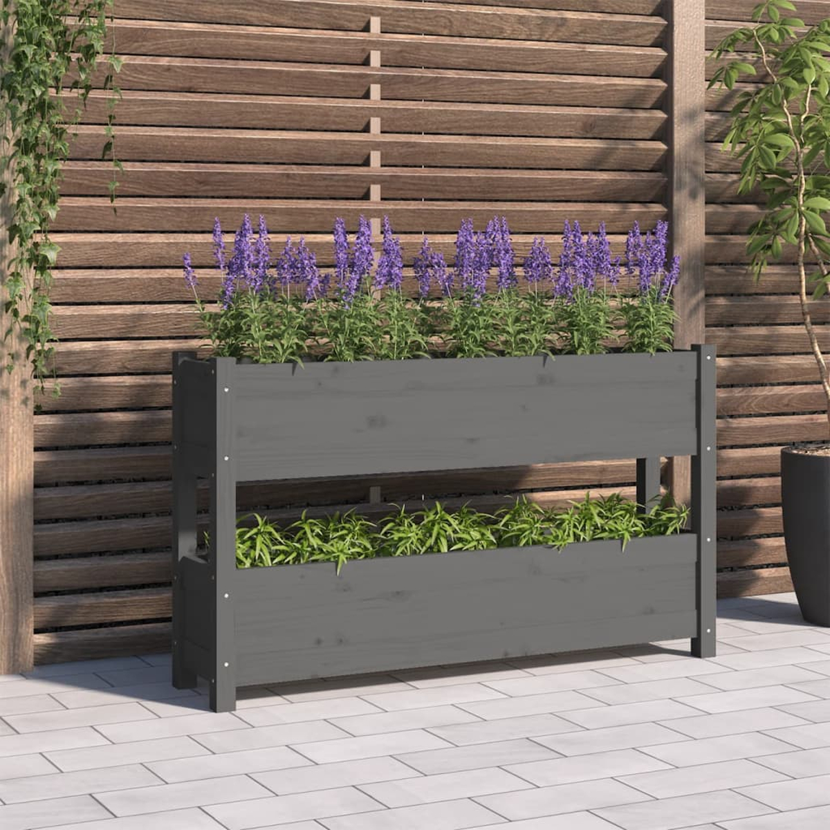 Ein dunkelgrauer Holzpflanzer mit zwei Ebenen von Blumen. Es ist im Freien, mit einem Holzzaun im Hintergrund.