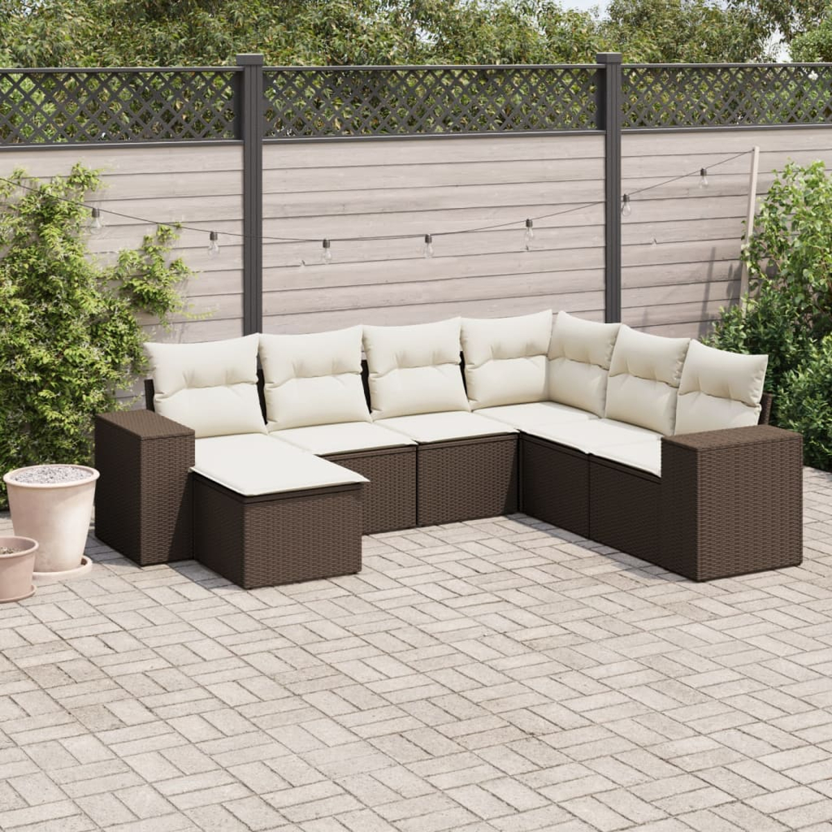 Ein braunes Outdoor-Sofa-Set mit cremefarbenen Kissen auf einer Ziegelterrasse. Pflanzen und Zaun im Hintergrund.