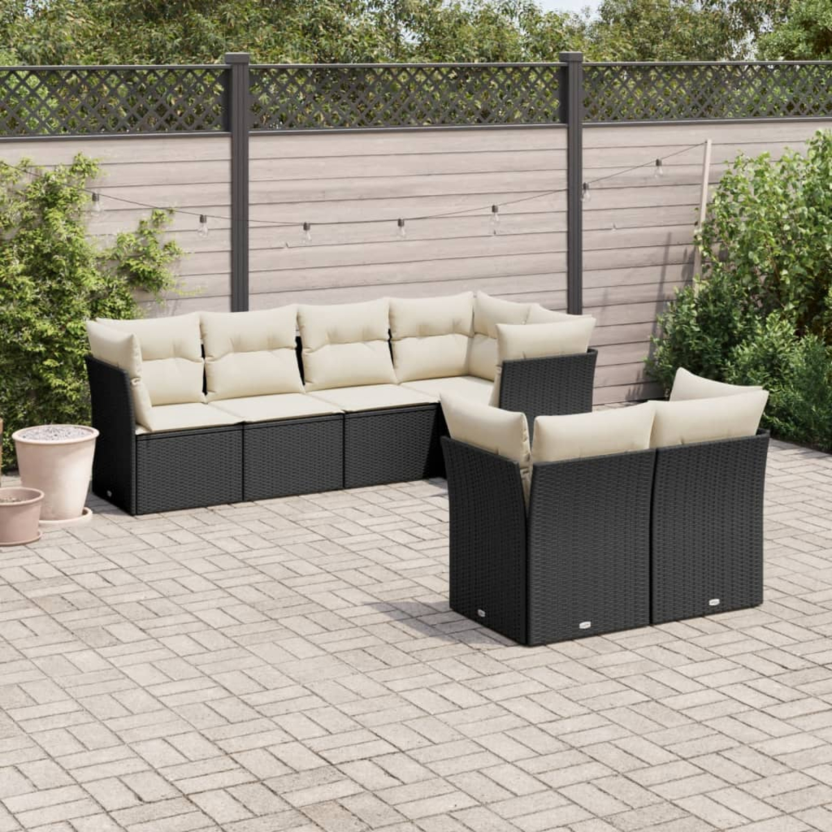 Ein schwarzes Rattan-Outdoor-Set mit cremefarbenen Kissen auf einer Ziegelterrasse. Es enthält ein Sofa und zwei Stühle.